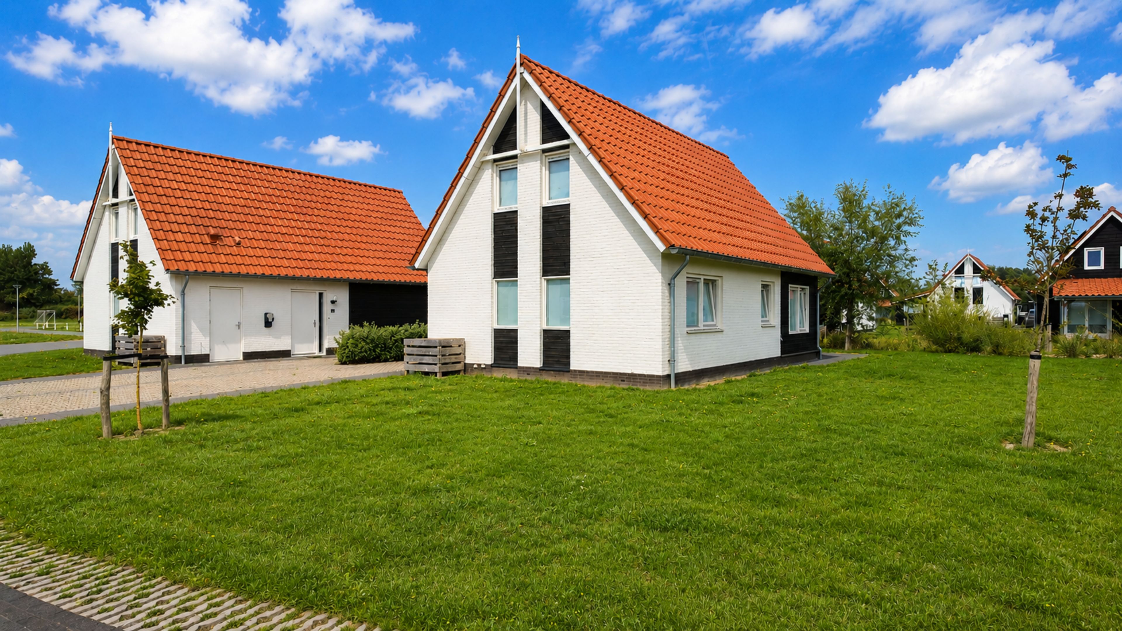 Dos casas blancas con tejados rojos y un césped verde.