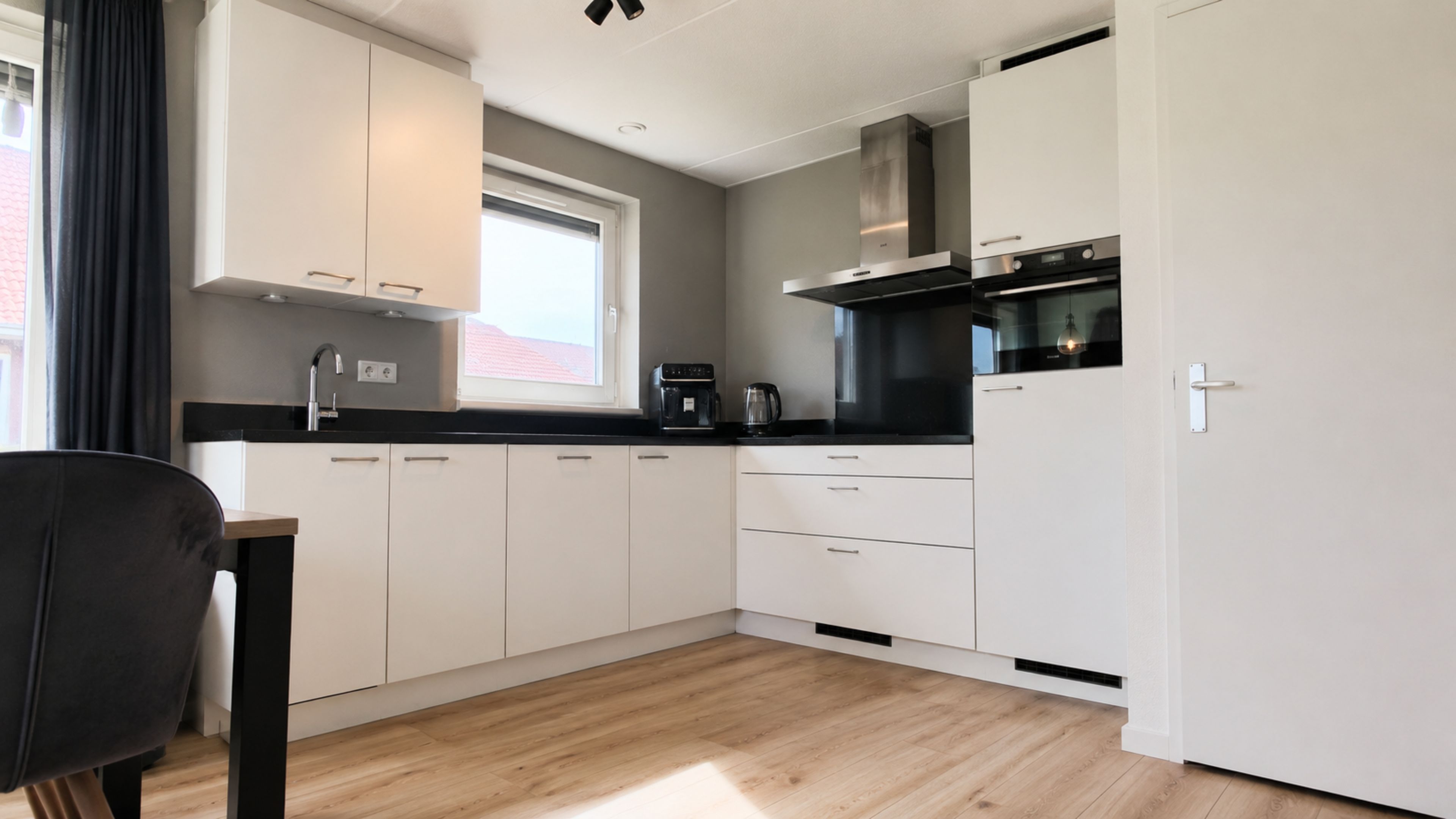 A modern kitchen with white cabinets, a black countertop, and a window.