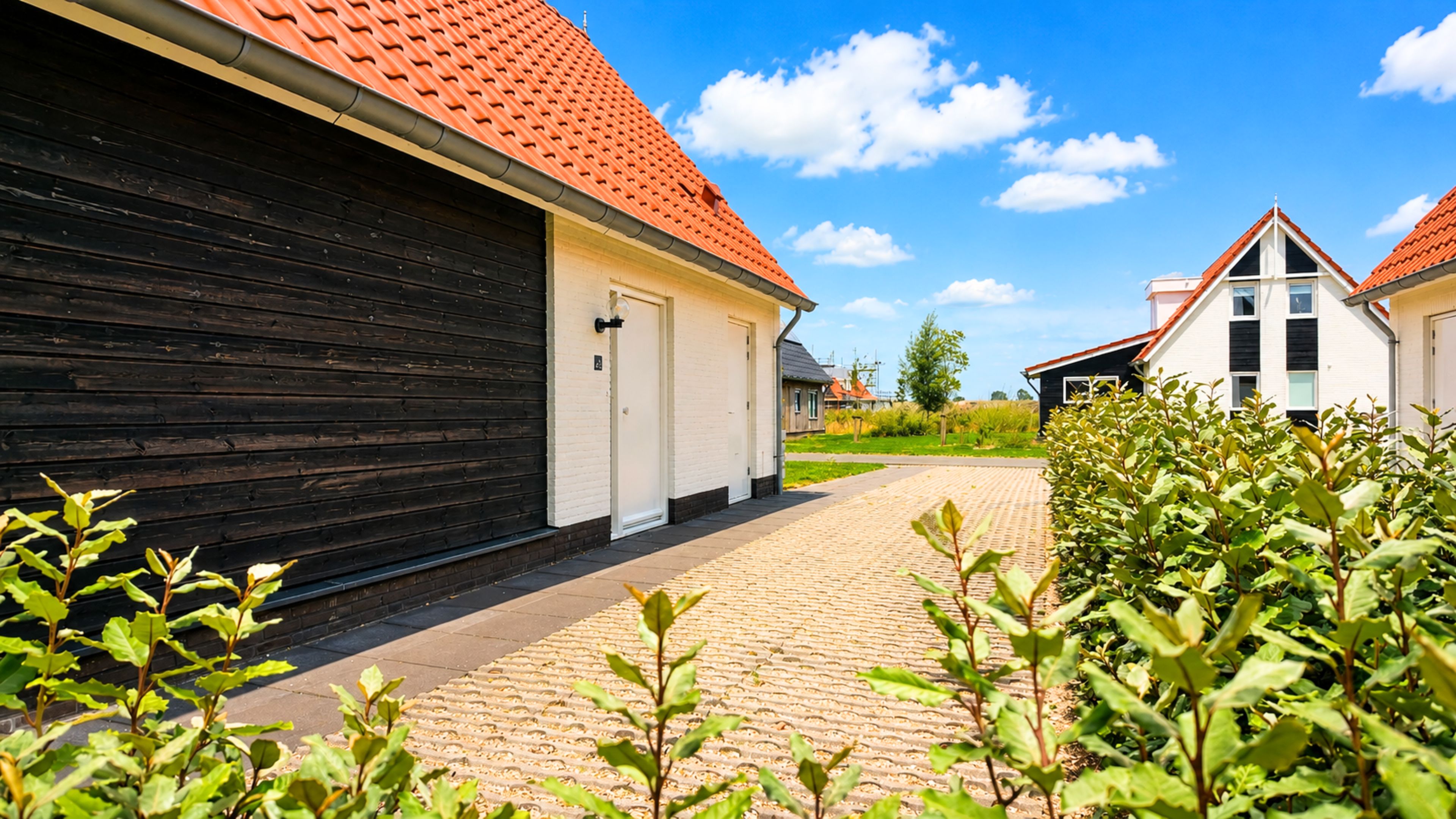 A building with a red-tiled roof, a black exterior wall, and a paved pathway leading to a white door.