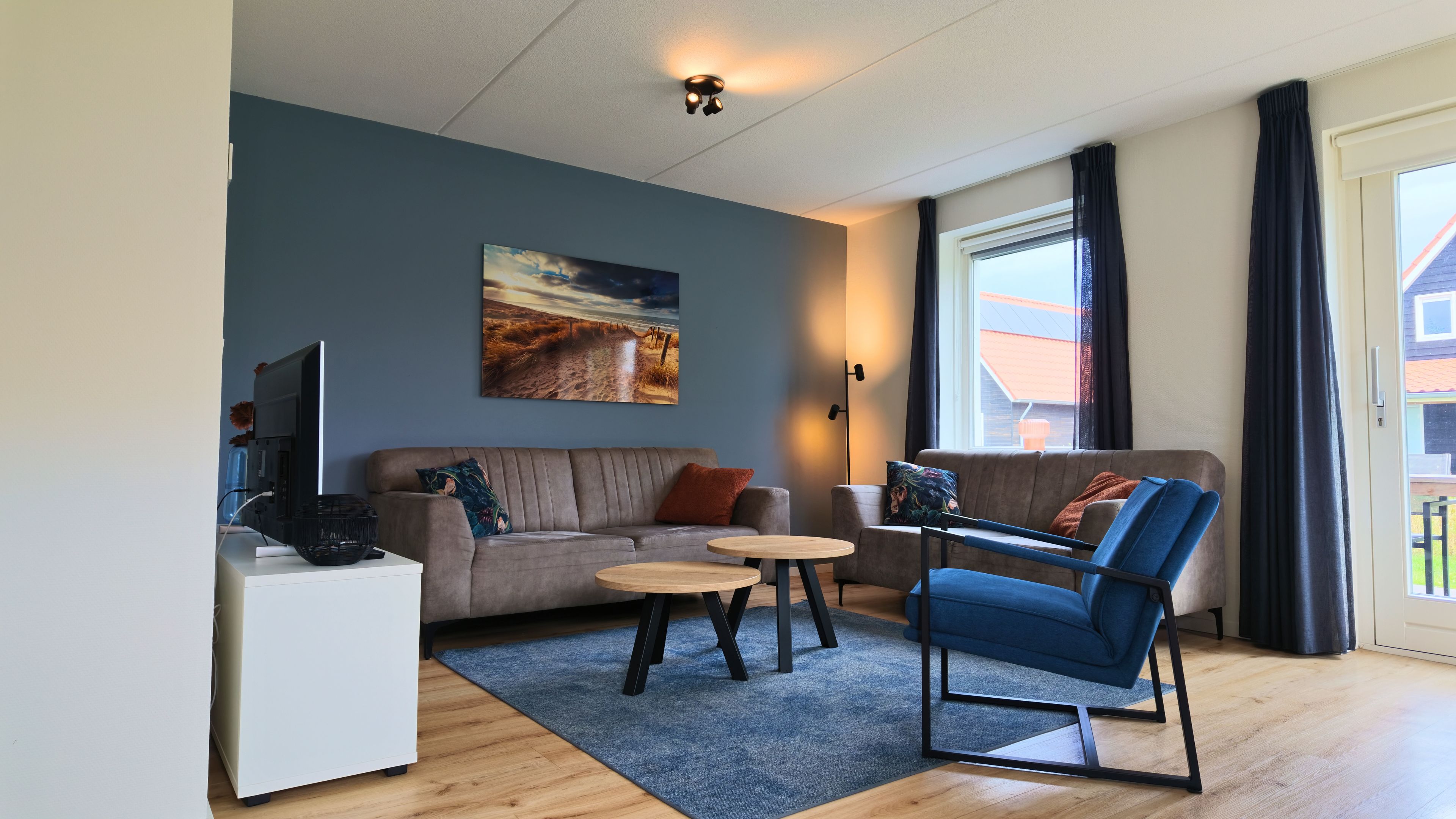 Een moderne woonkamer met een bank, twee bijzettafeltjes, een televisie en een schilderij aan de muur.