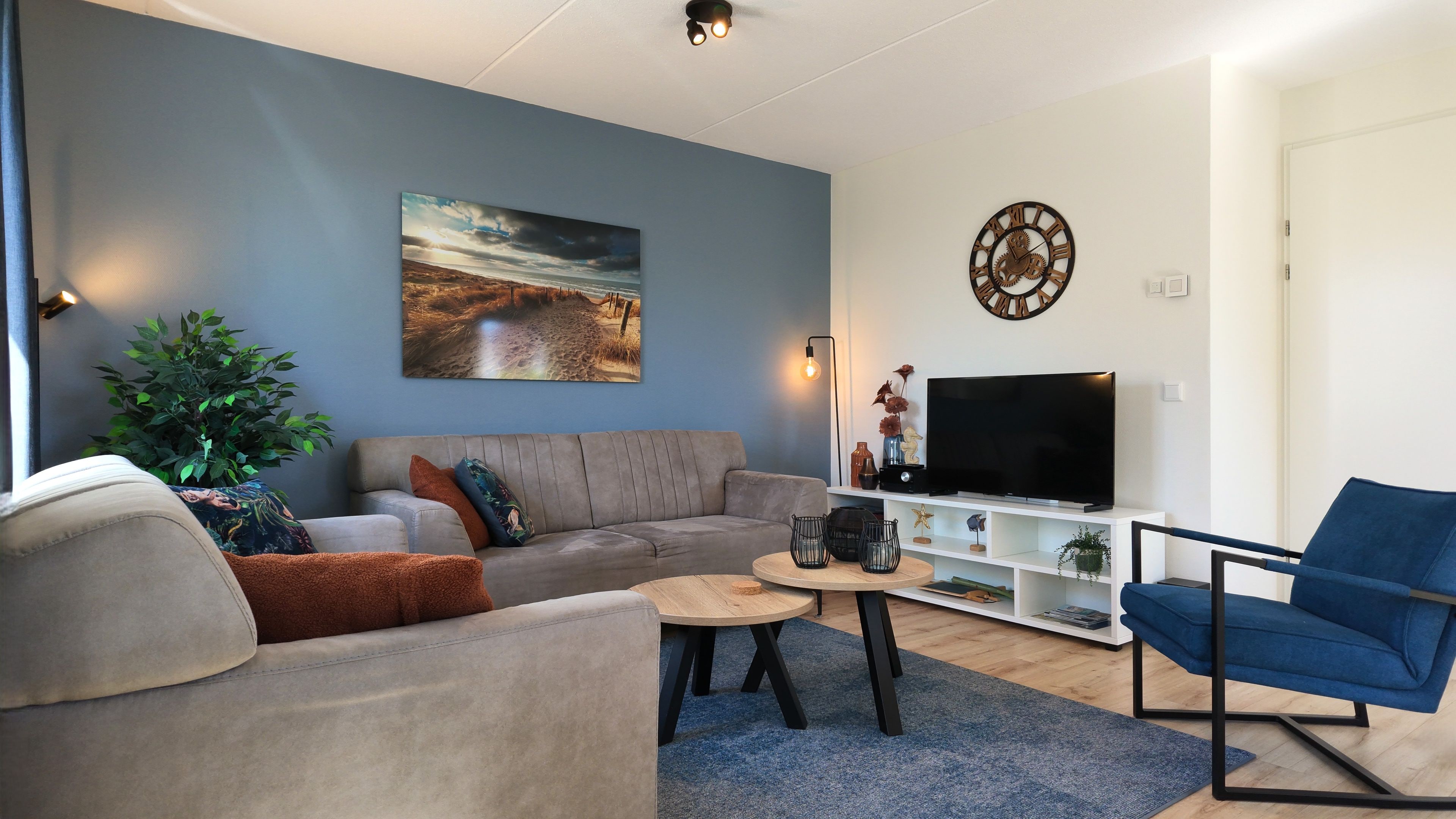 Ein modernes Wohnzimmer mit einem grauen Sofa, einem blauen Sessel, einem Flachbildfernseher und einem Gemälde an der Wand.