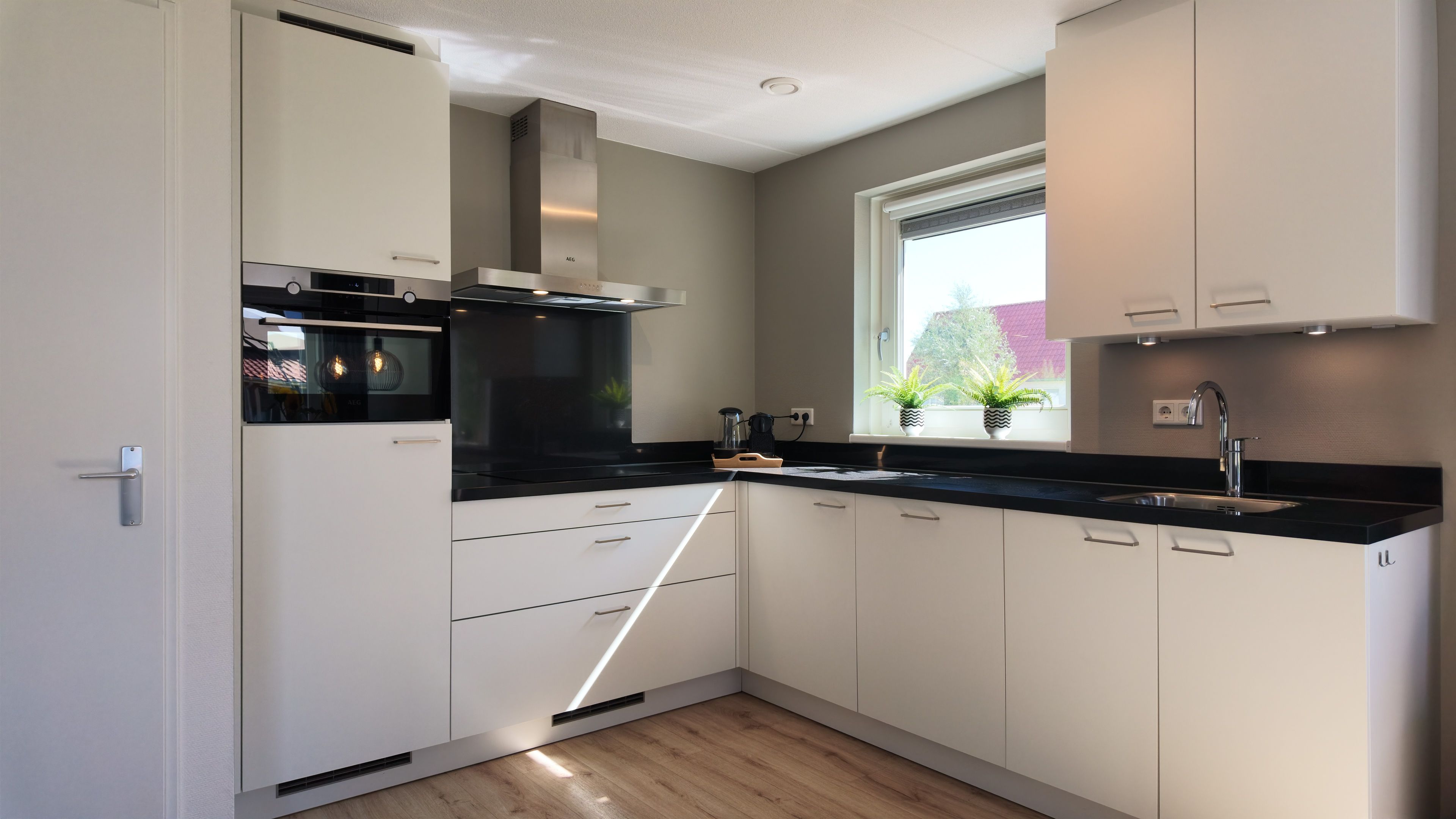 A modern kitchen with white cabinetry, a black countertop, and a window with potted plants.