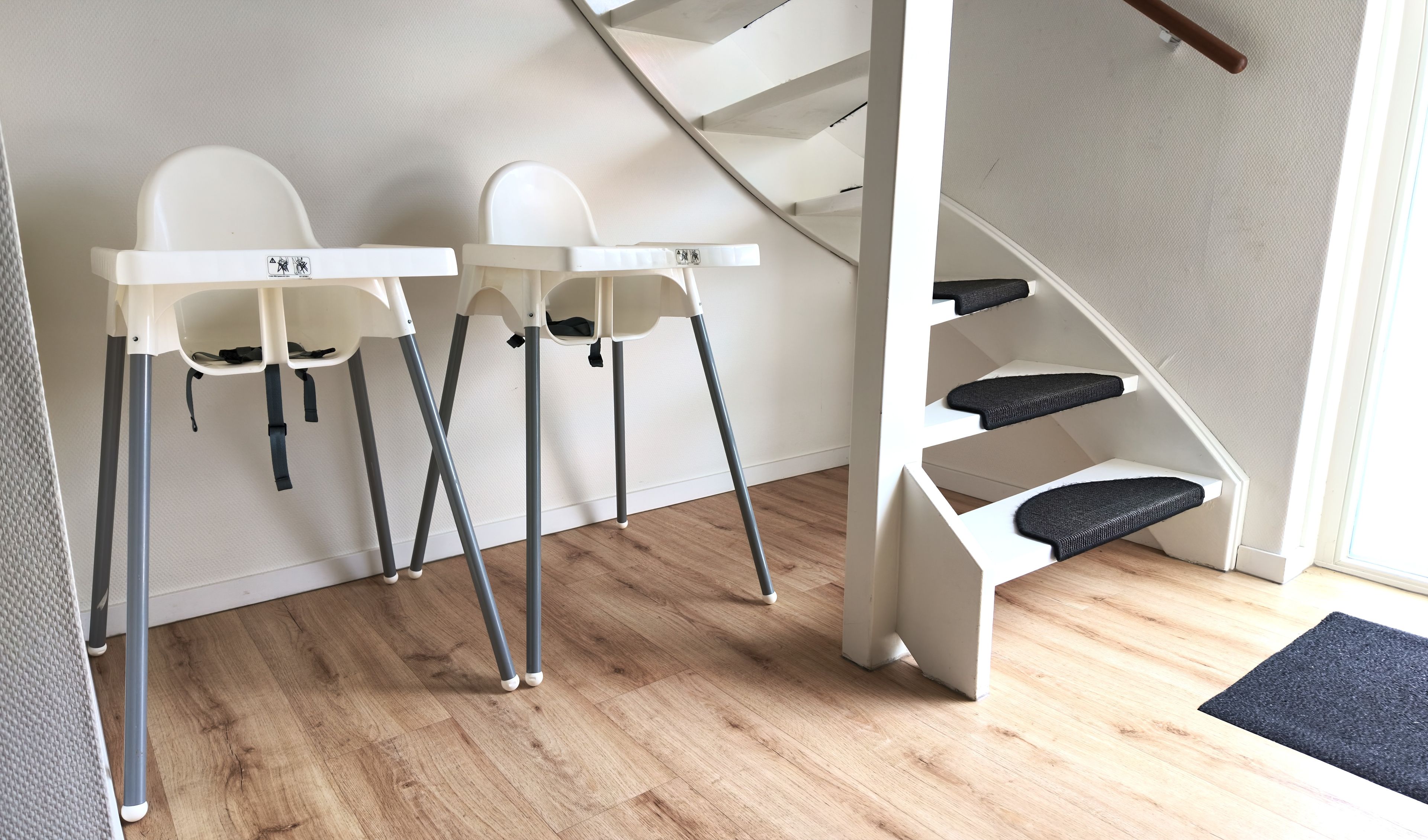 Een kamer met een houten vloer, witte wanden en een witte trap met zwarte treden.