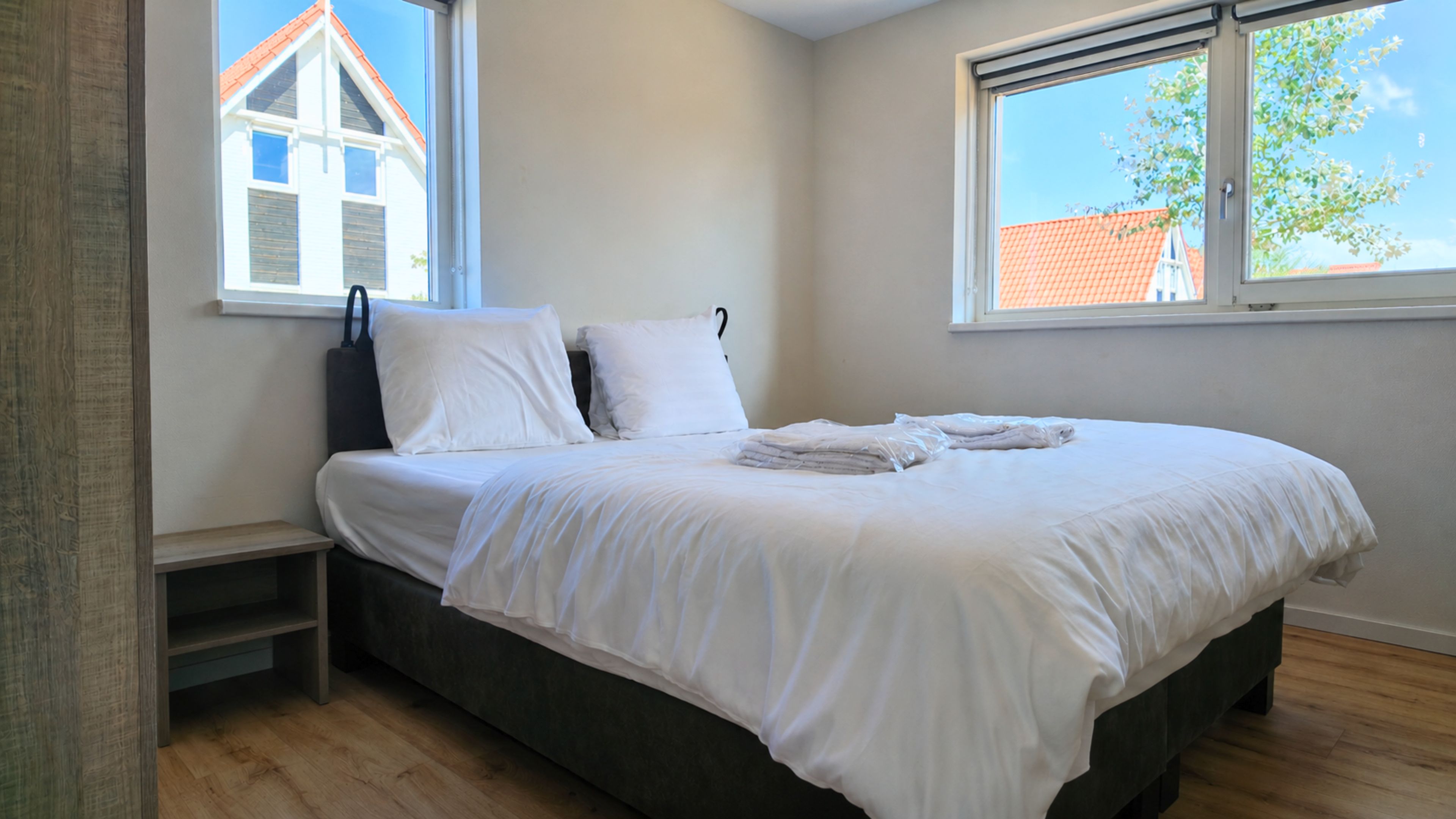 Une chambre à coucher avec un lit, des oreillers, une fenêtre et une vue sur un bâtiment à l’extérieur.