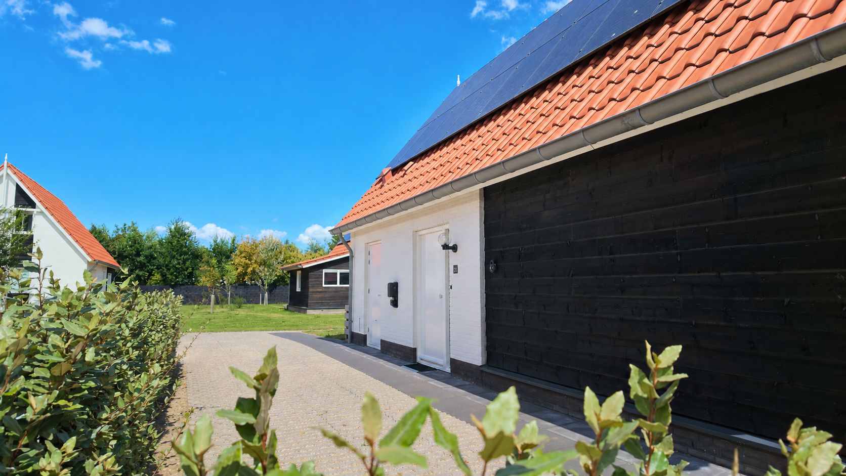 Un quartiere residenziale con vialetto lastricato che conduce a una casa con tetto in tegole rosse e porta bianca.