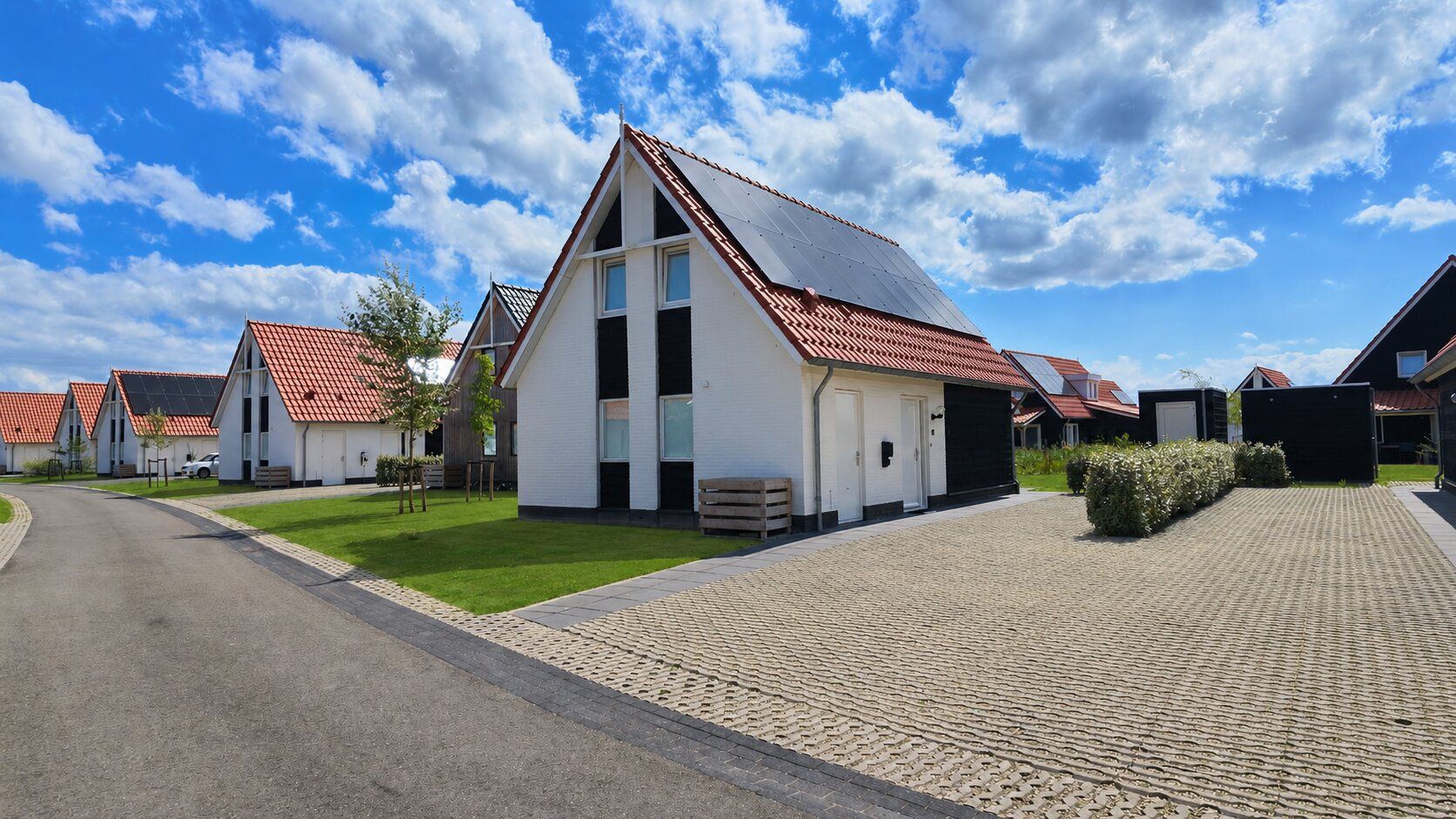 A row of white buildings with red roofs, a paved driveway, and a clear blue sky.