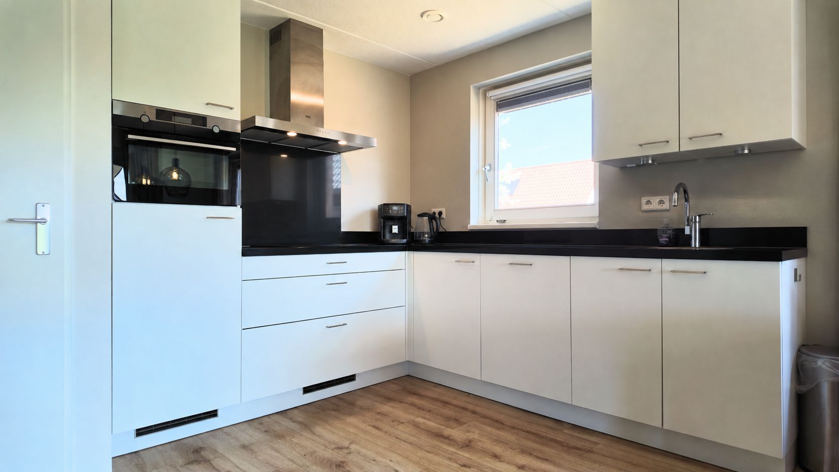 A modern kitchen with white cabinetry, a black countertop, and a window above the sink.