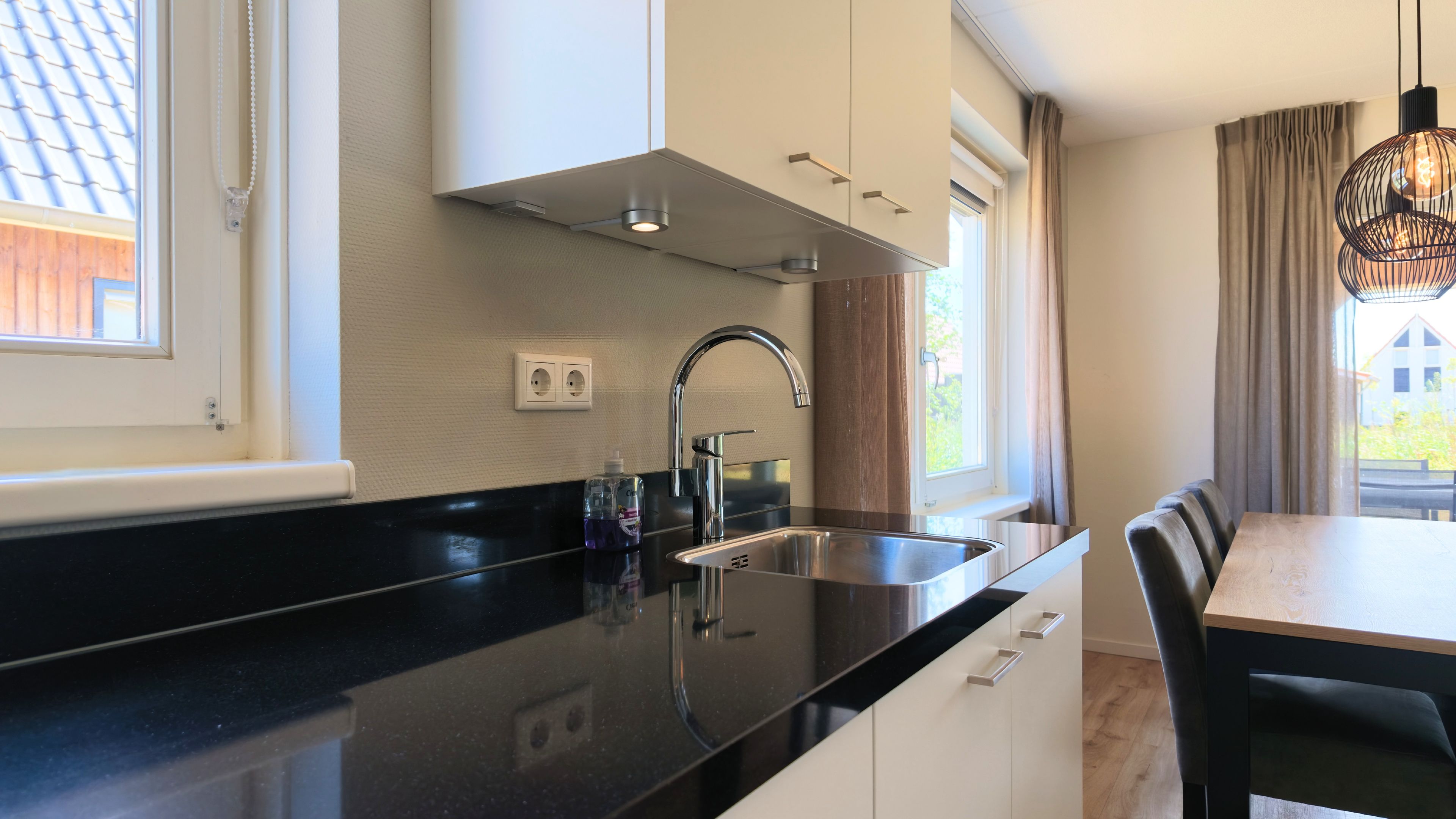 Una cucina moderna con piano di lavoro nero, lavello in acciaio inossidabile e mobili bianchi.