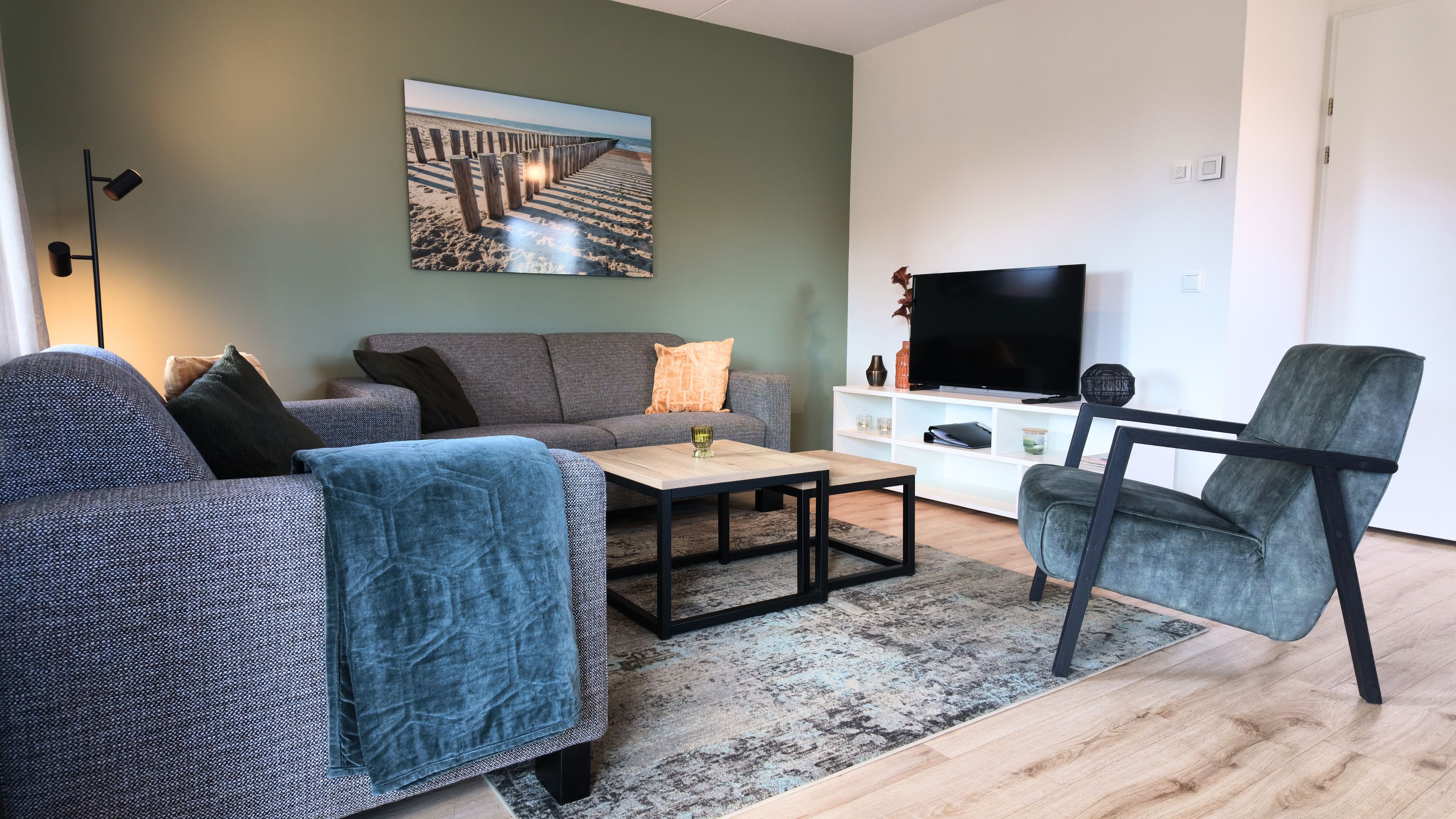 A modern living room with a sofa, armchair, coffee table, and a flat-screen TV.