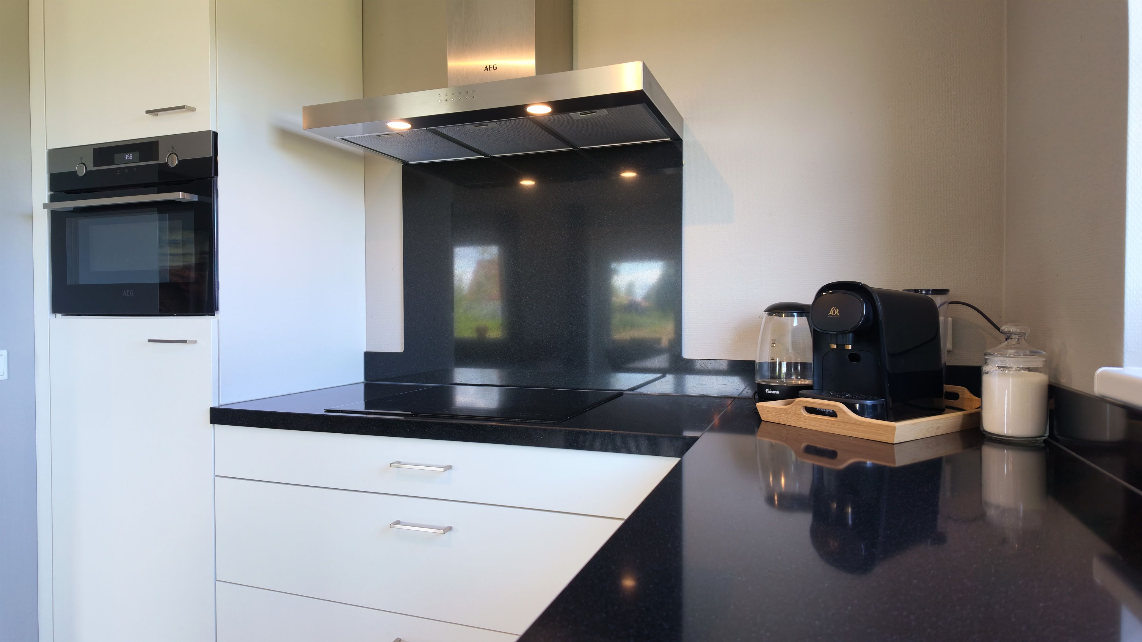 Una cocina moderna con horno empotrado, cafetera y un tarro de vidrio sobre la encimera.