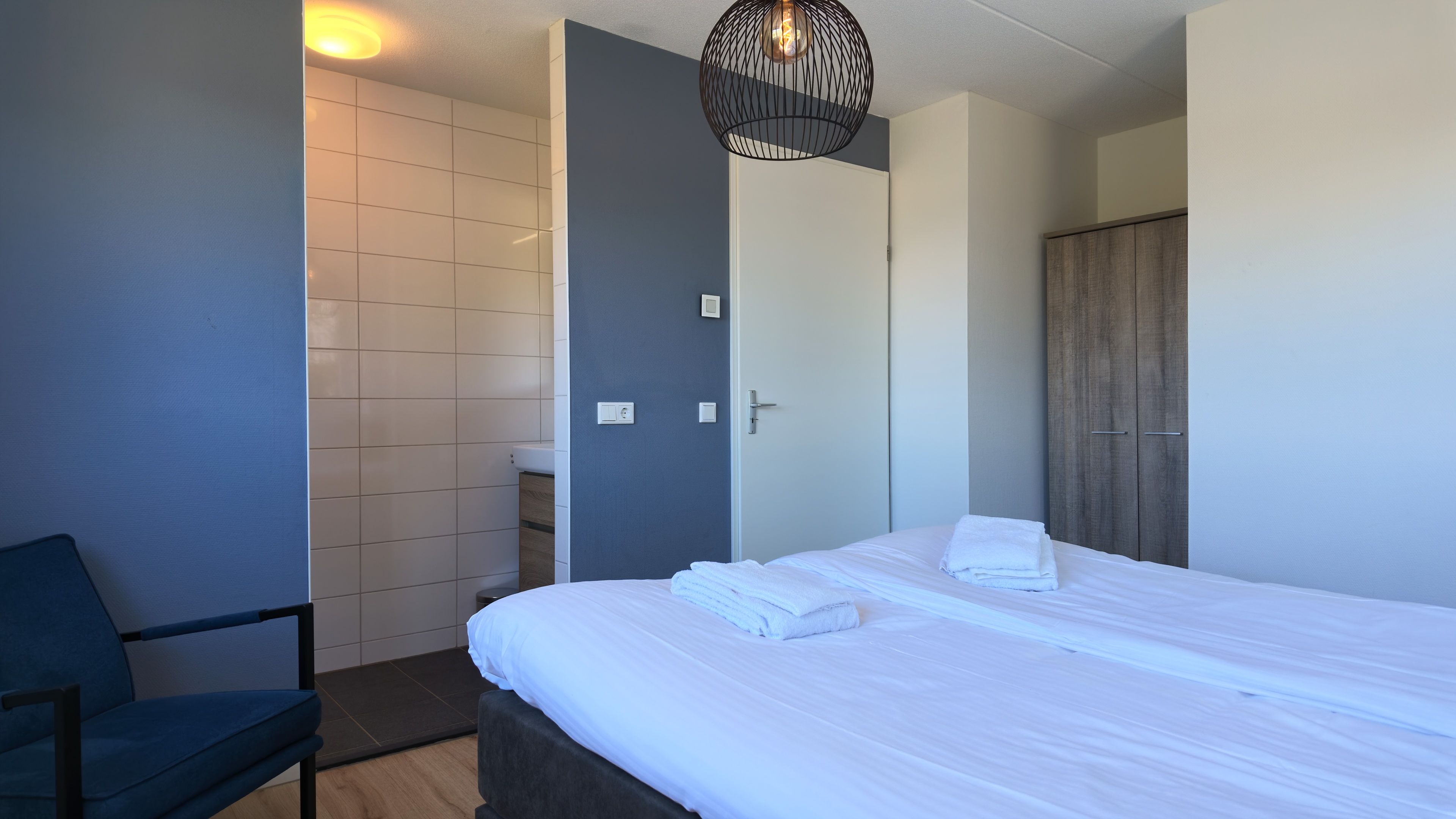 Una camera d'albergo con un letto, una sedia, un armadio e un bagno.