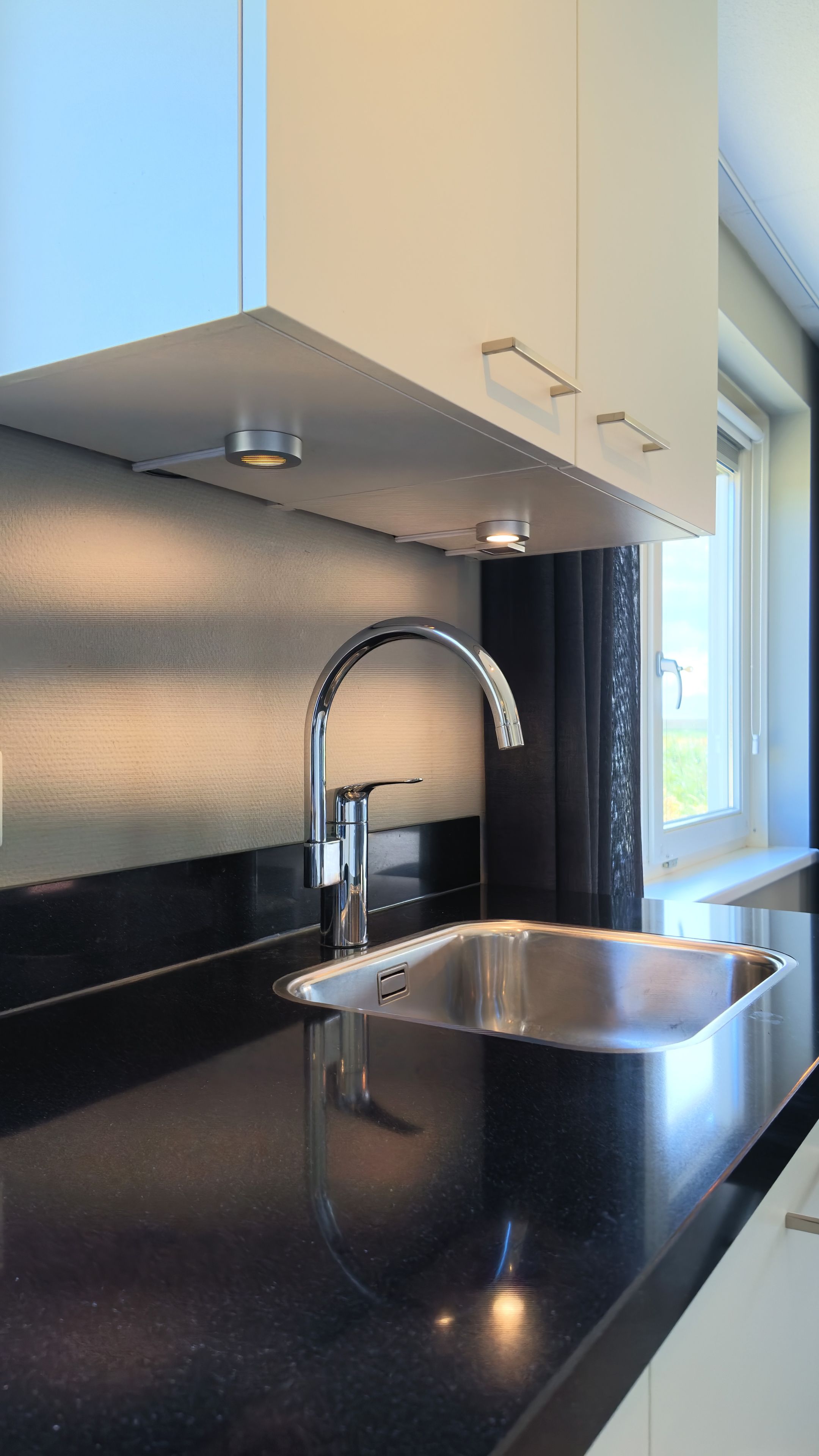 Una cucina moderna con lavello in acciaio inossidabile, un rubinetto a collo di cigno e una finestra vista verde.