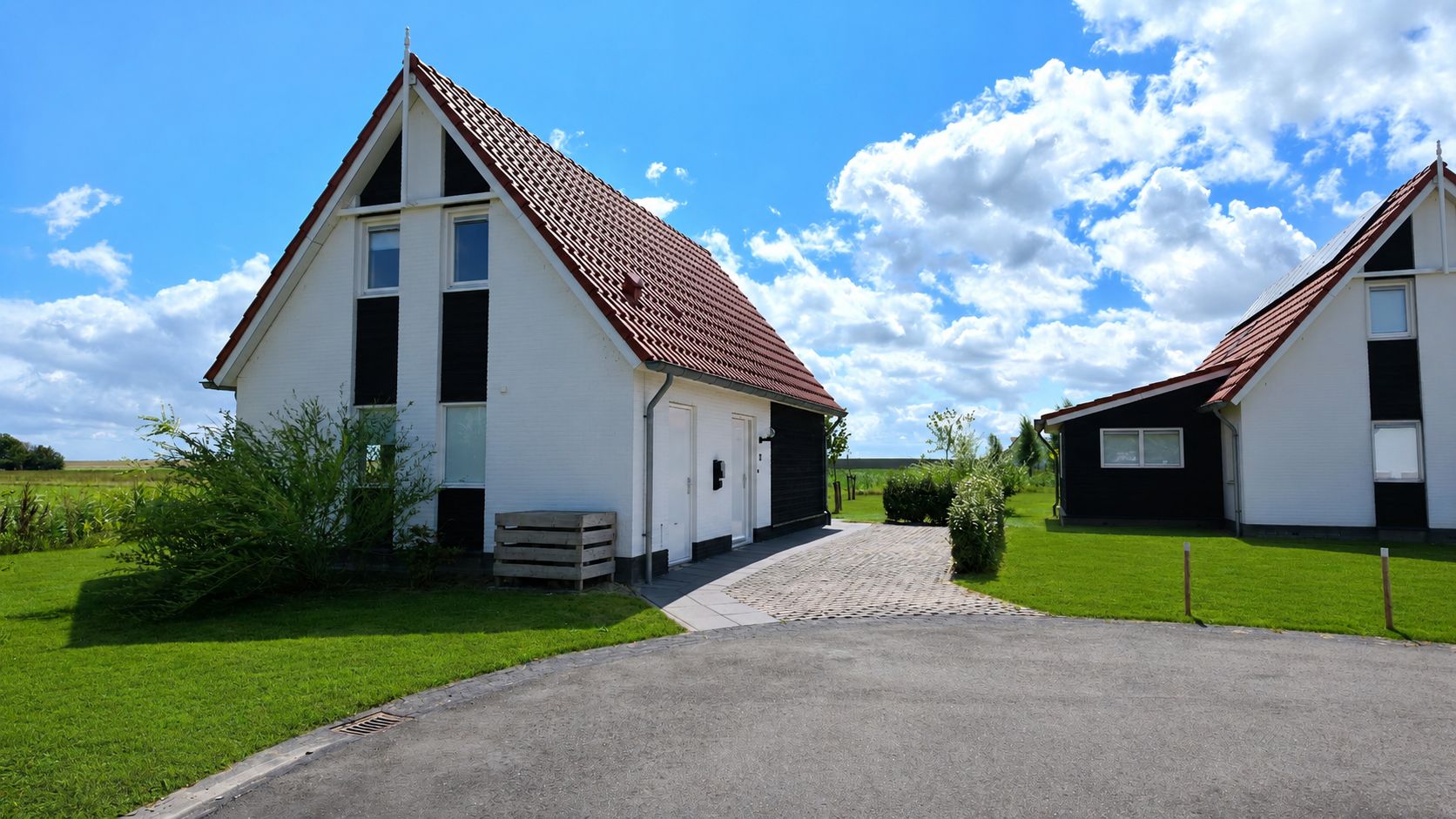 Two single-story buildings with red roofs, a paved driveway, and a grassy area with a small bush.