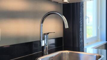 Een moderne keuken met een roestvrijstalen spoelbak, een gebogen kraan en een raam met uitzicht op groen.