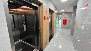 Um elevador moderno com acabamento metálico e painel de madeira, acompanhado de botões de emergência vermelhos e indicação clara do andar.