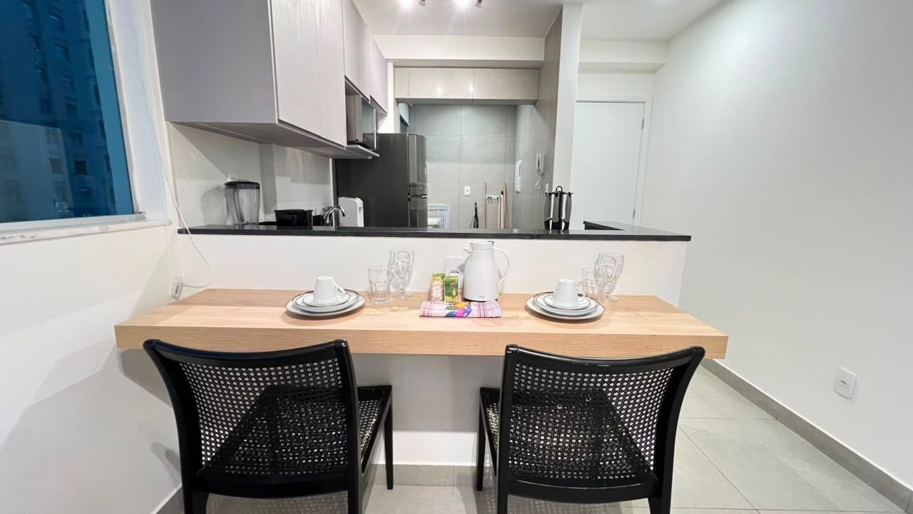 Une cuisine moderne avec un plan de travail en bois, deux chaises noires et une table à manger dressée pour deux personnes.