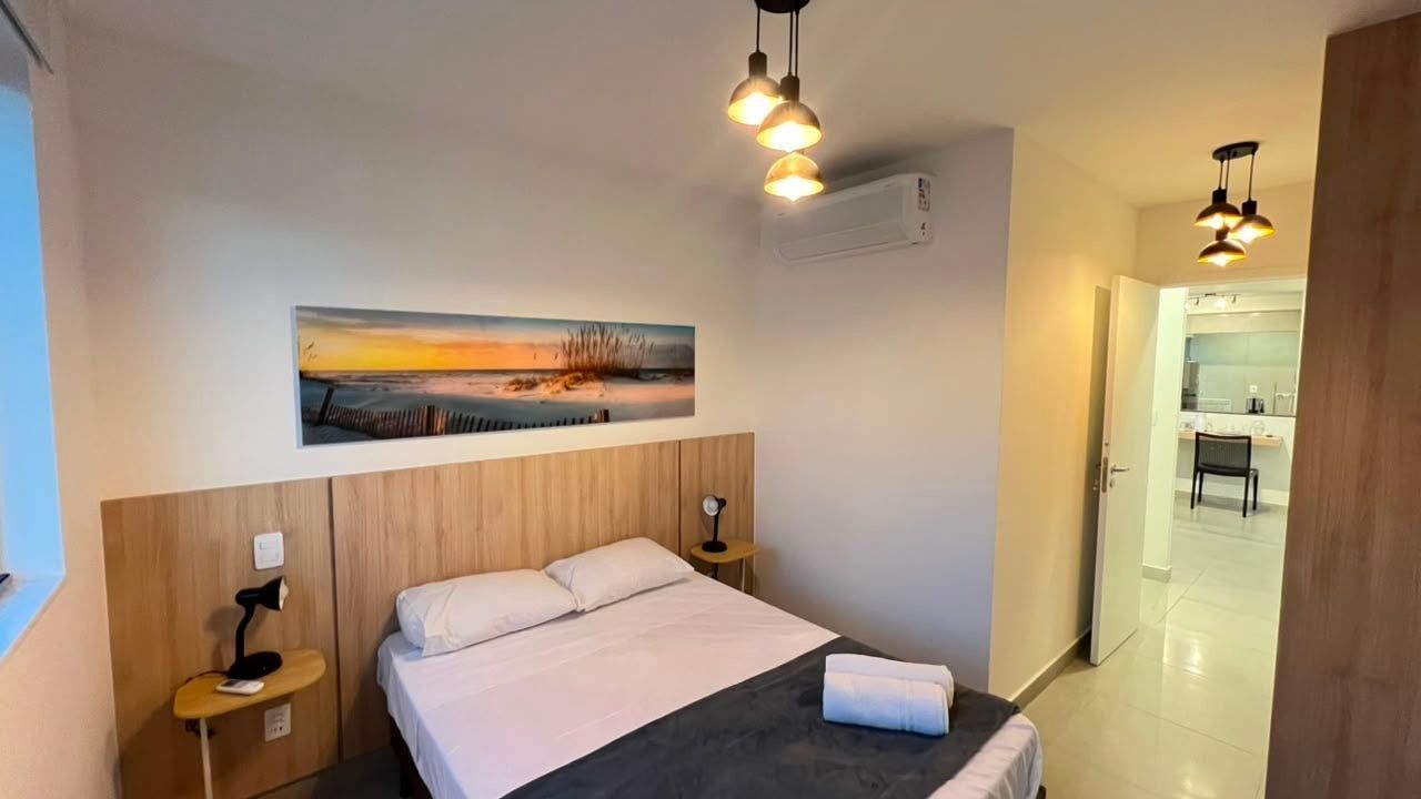 Habitación de hotel con cama, lámparas de noche, un cuadro y vista al baño.