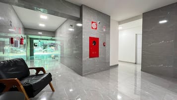 Un vestíbulo moderno con suelo de mármol, un letrero de salida de emergencia en rojo y un escaparate de vidrio al fondo.