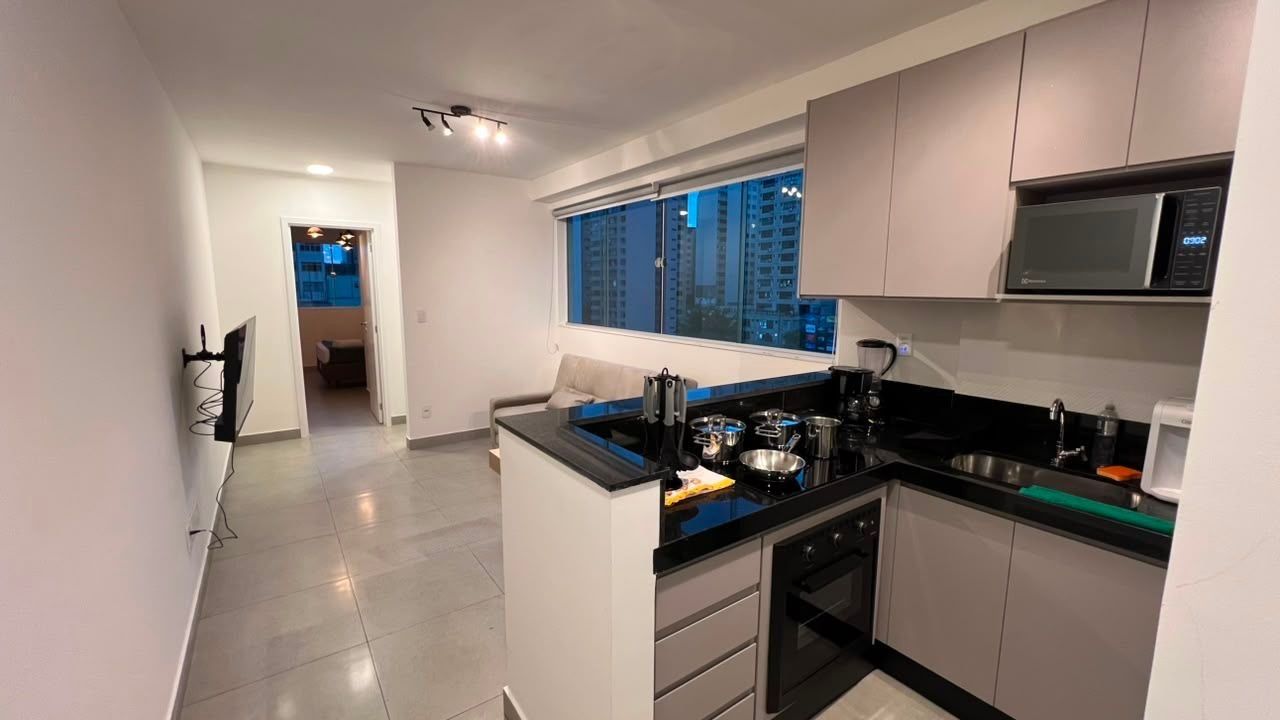 Cozinha moderna com bancada preta, eletrodomésticos de aço inoxidável e janela com vista para a cidade.