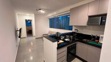 Cozinha moderna com bancada preta, eletrodomésticos de aço inoxidável e janela com vista para a cidade.