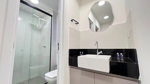 Une salle de bain moderne avec une douche à parois de verre, des toilettes blanches et un lavabo noir sur un plan de travail, avec un miroir au-dessus.