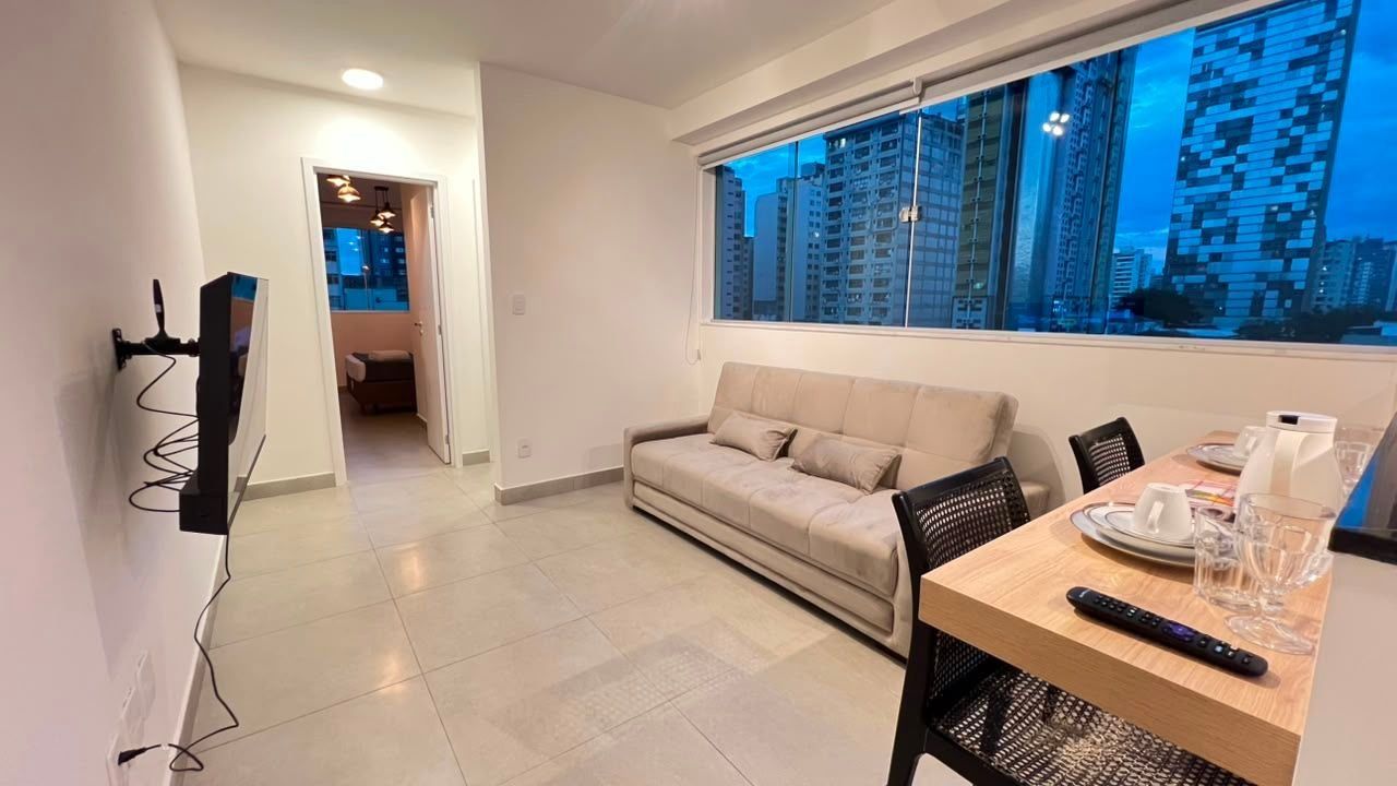Una sala de estar moderna con sofá, mesa de comedor con sillas, televisor y ventana con vista a la ciudad.