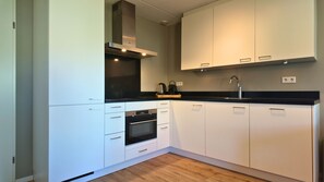 A modern kitchen with white cabinetry, a black countertop, and a stainless steel range hood. - Looking for a holiday home in Zeeland for 8 people? Discover Villa De Merel, featuring four bedrooms, three bathrooms and a covered terrace. (Scherpenisse)