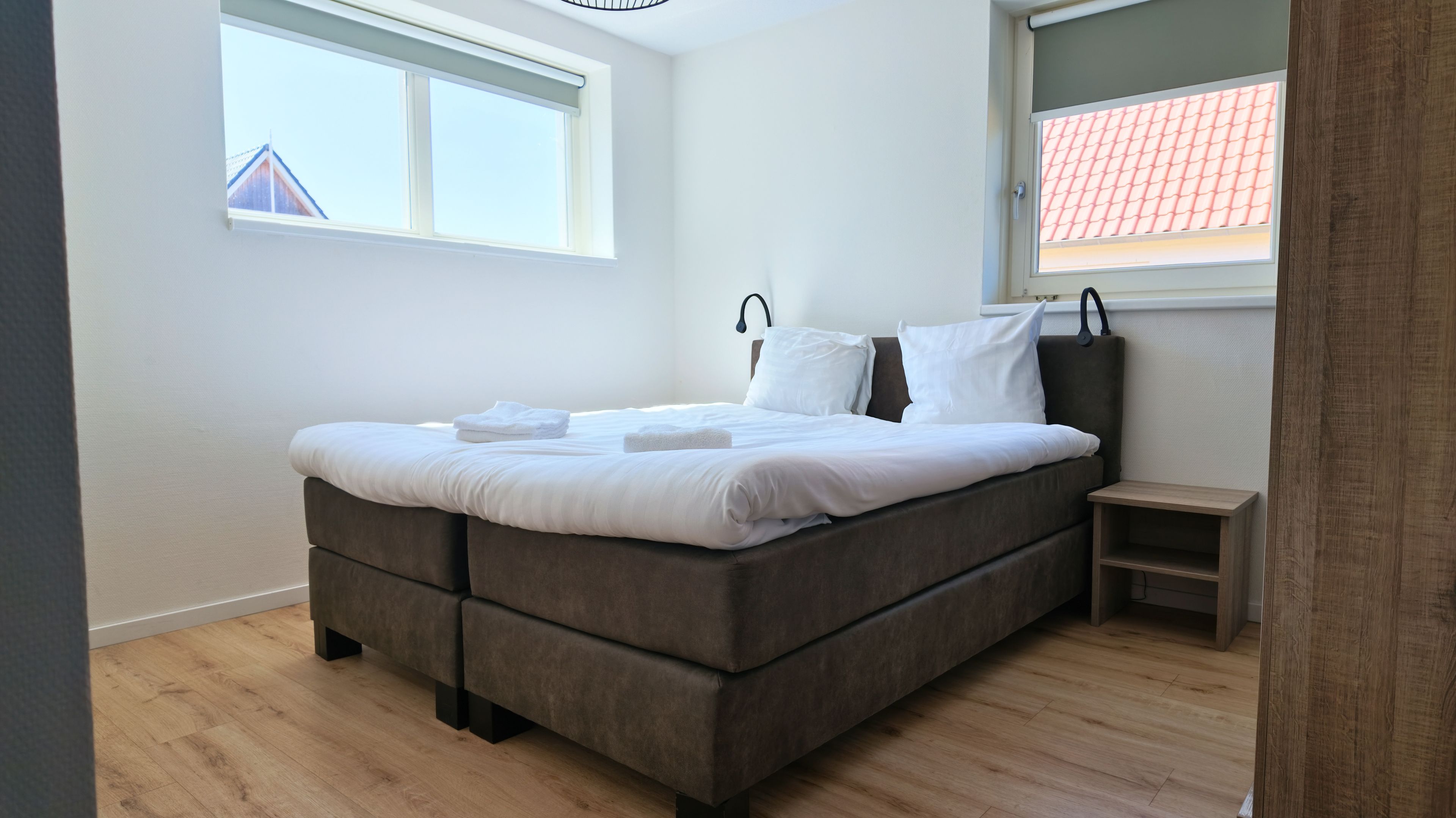 Una camera da letto con un letto, un comodino, una finestra e vista su un edificio.