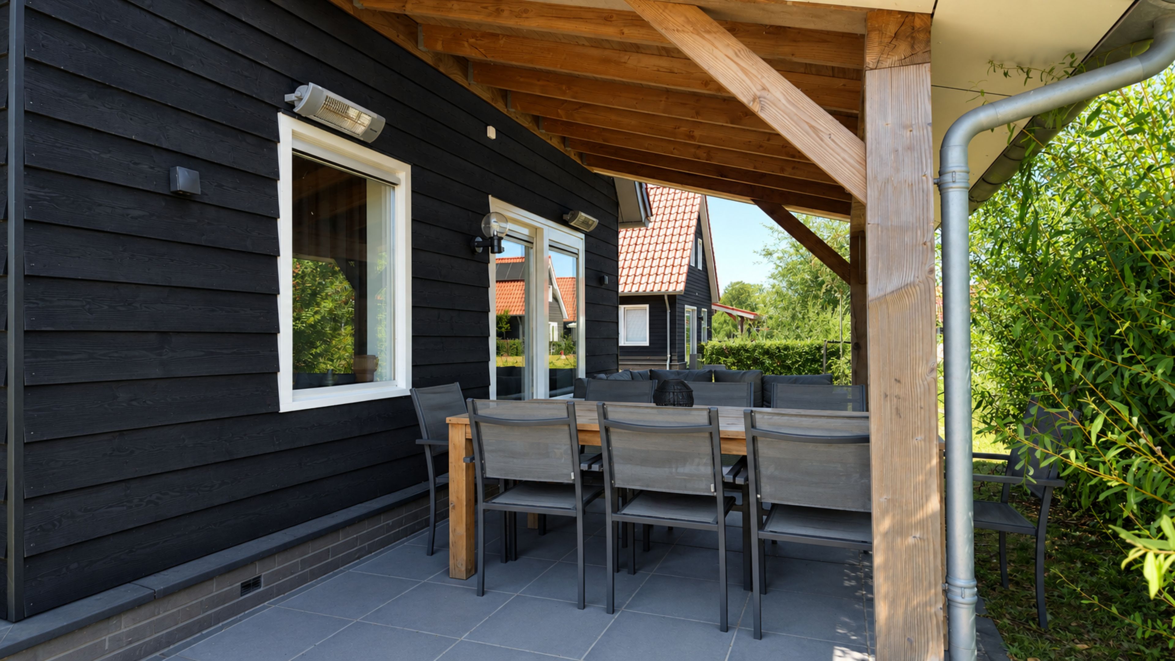 Una terrazza esterna con tavolo e sedie, un soffitto in legno e vista su una casa con tetto rosso.