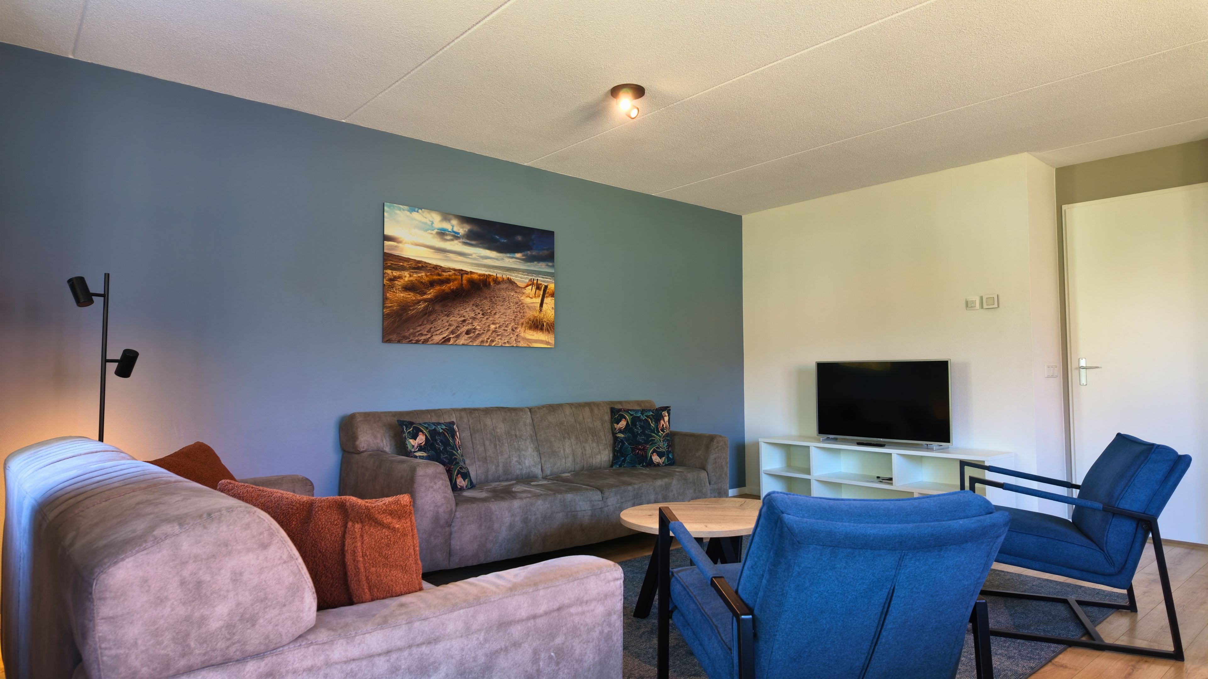 A living room with a sofa, armchairs, a coffee table, a flat-screen TV, and a painting on the wall.