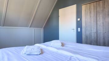 Una camera da letto con un letto, lenzuola bianche, un armadio in legno e una porta con l'interruttore della luce.