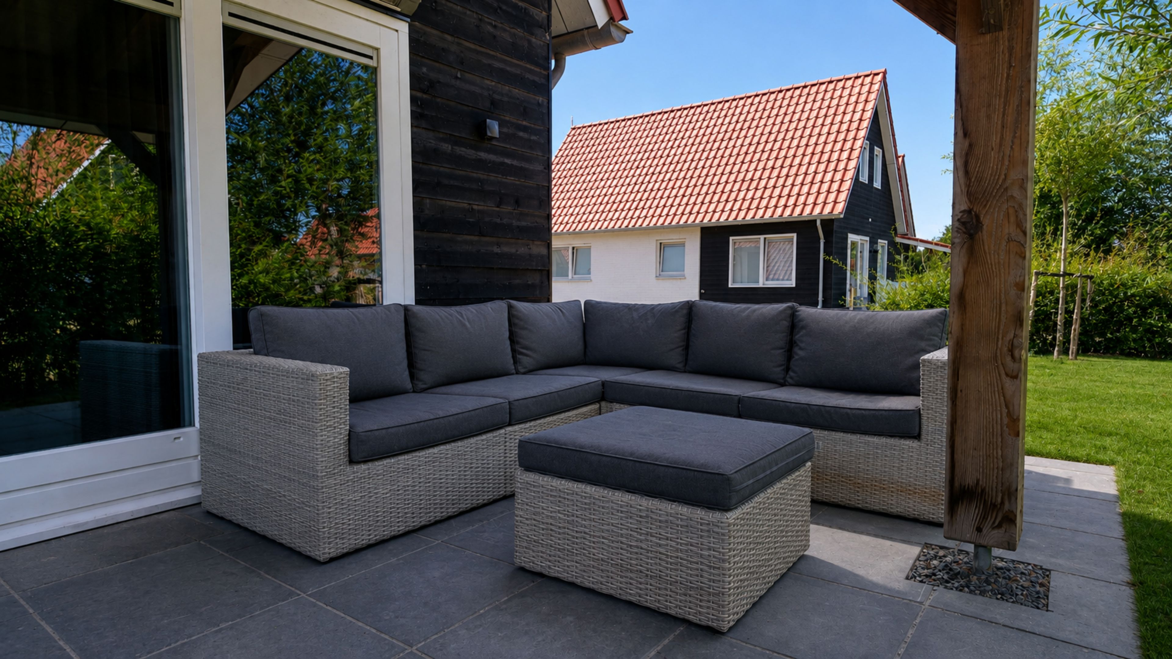 A sectional sofa with a matching ottoman on a patio with a view of a house.