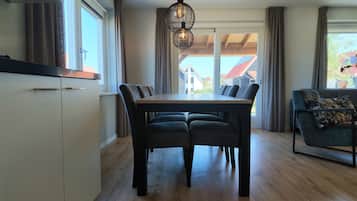 Een eethoek met een tafel en stoelen, een keuken met kastjes, en uitzicht op een huis door een raam.