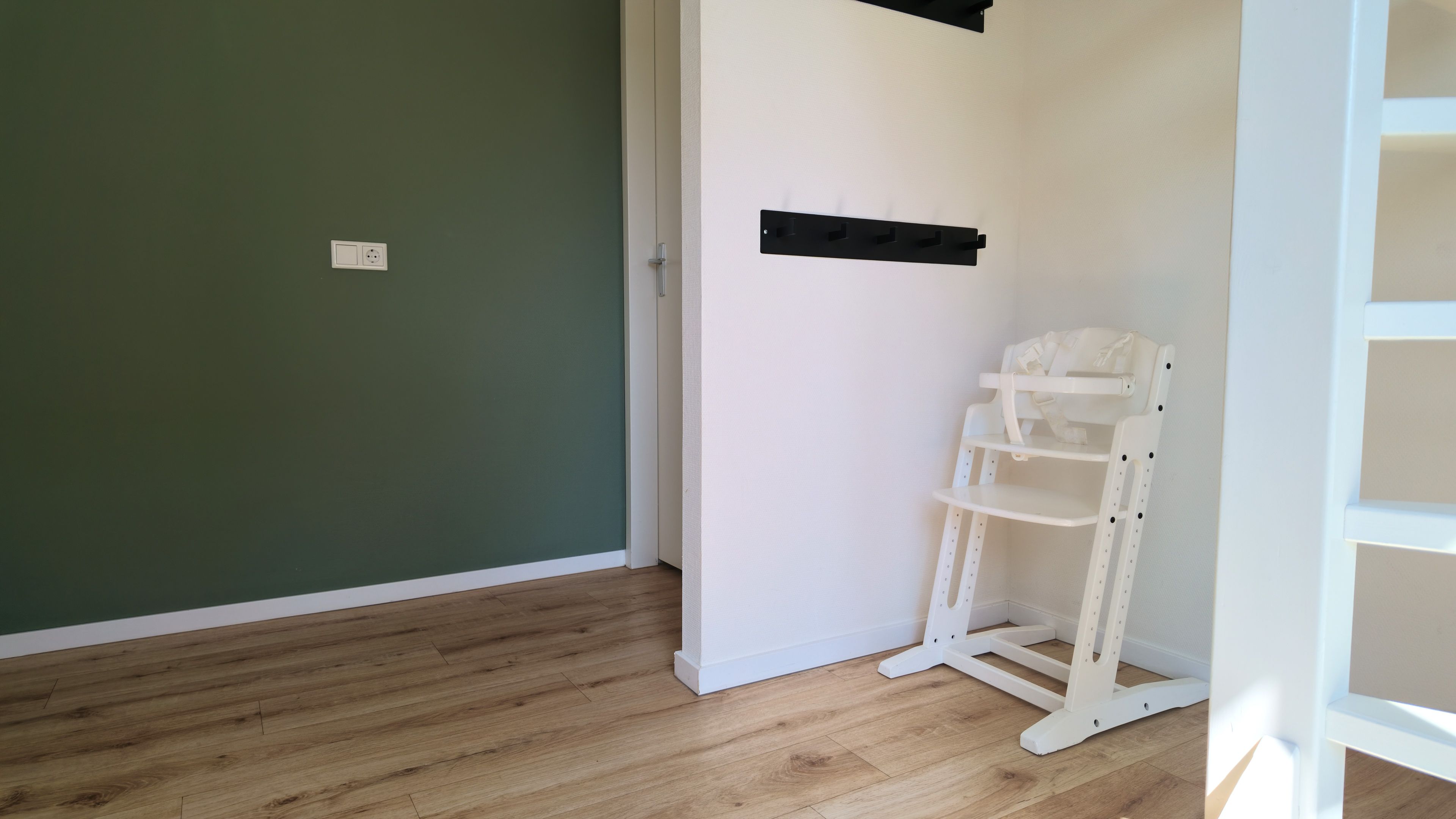 Une pièce avec un plancher en bois, une chaise blanche et une étagère blanche adossée à un mur vert.
