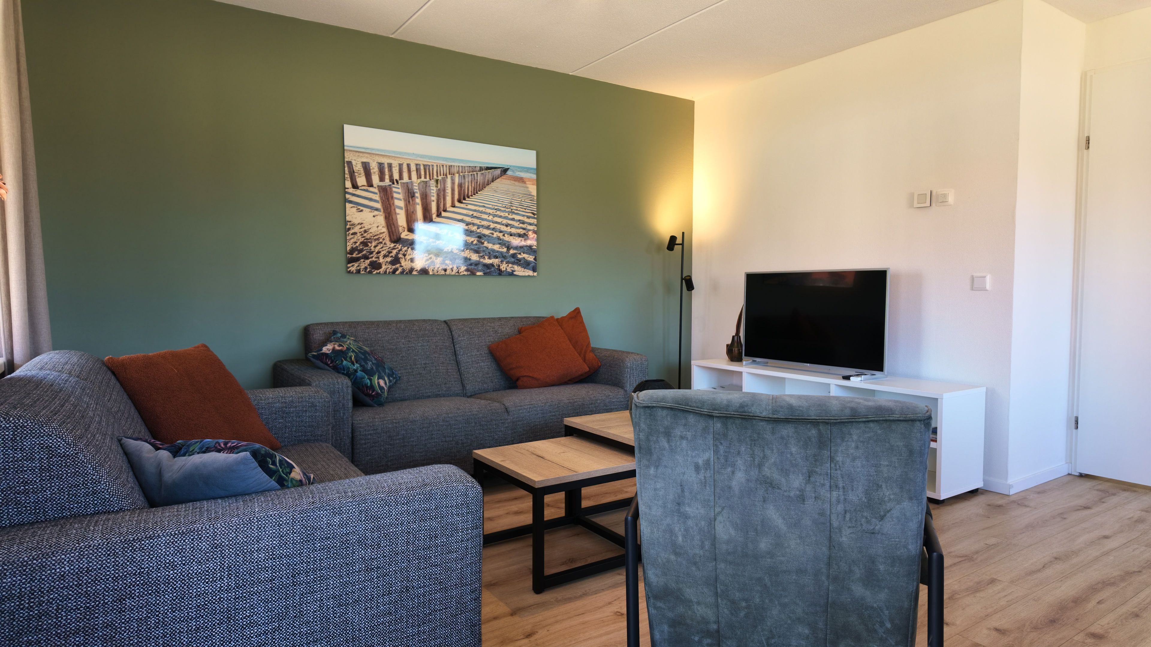 Een woonkamer met een bank, een salontafel, een televisie op een dressoir en een schilderij aan de muur.