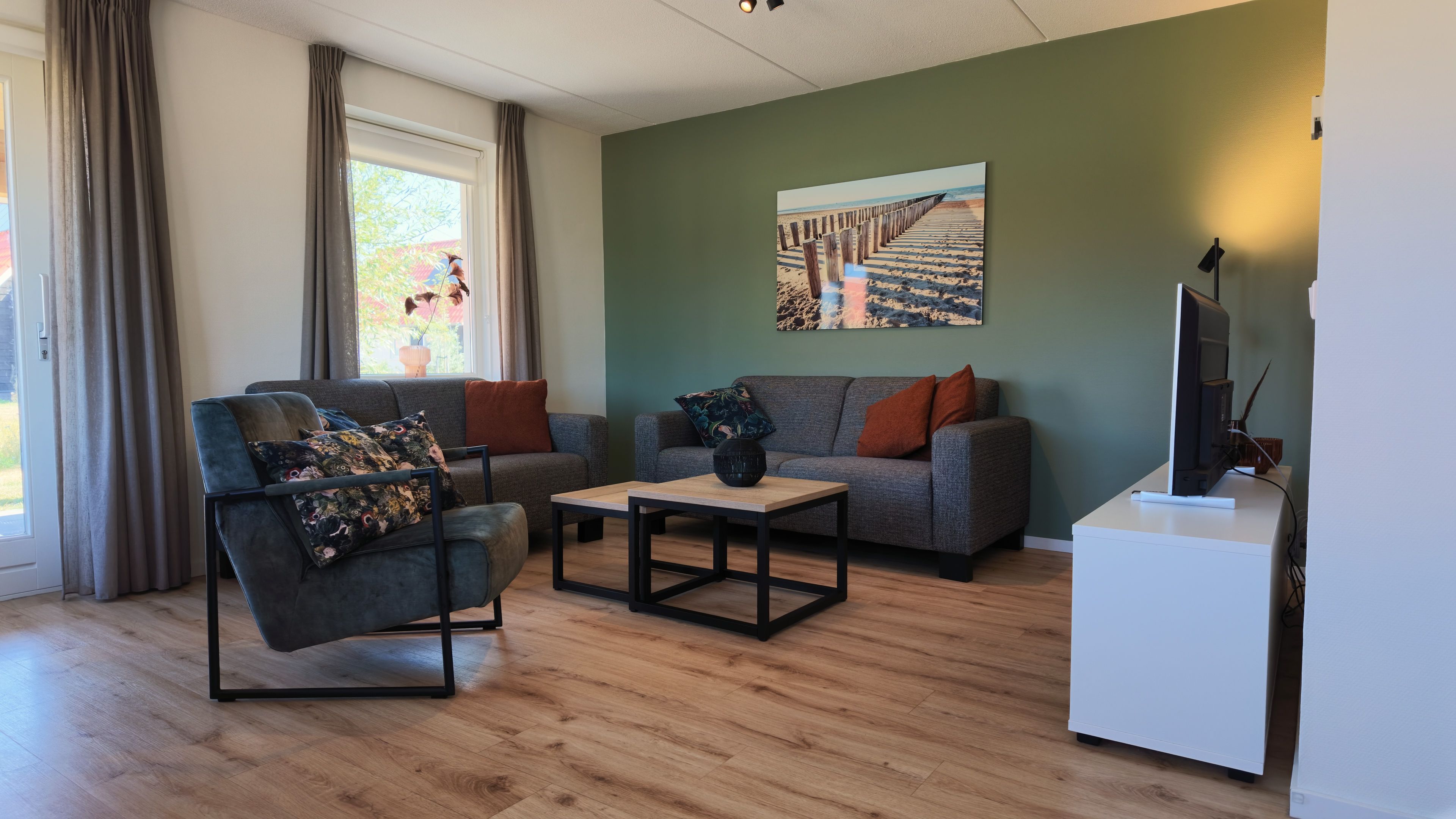 A modern living room with a sofa, armchair, coffee table, and a flat-screen TV.