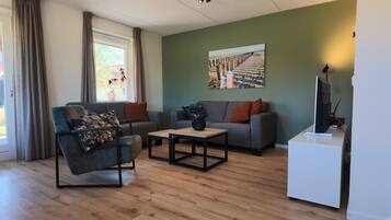 A modern living room with a sofa, armchair, coffee table, and a flat-screen TV.
