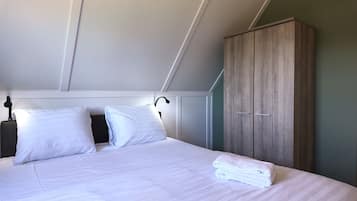 A neatly made bed with white linens, a wooden wardrobe, and a bedside lamp.