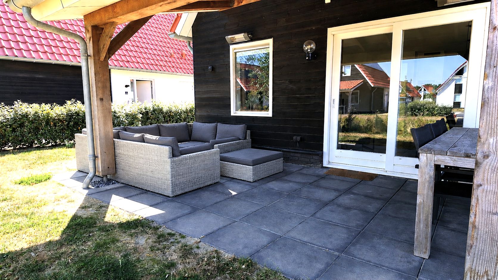 Una veranda esterna con un divano in vimini, un tavolo di legno e una porta vetrata che dà su un giardino.