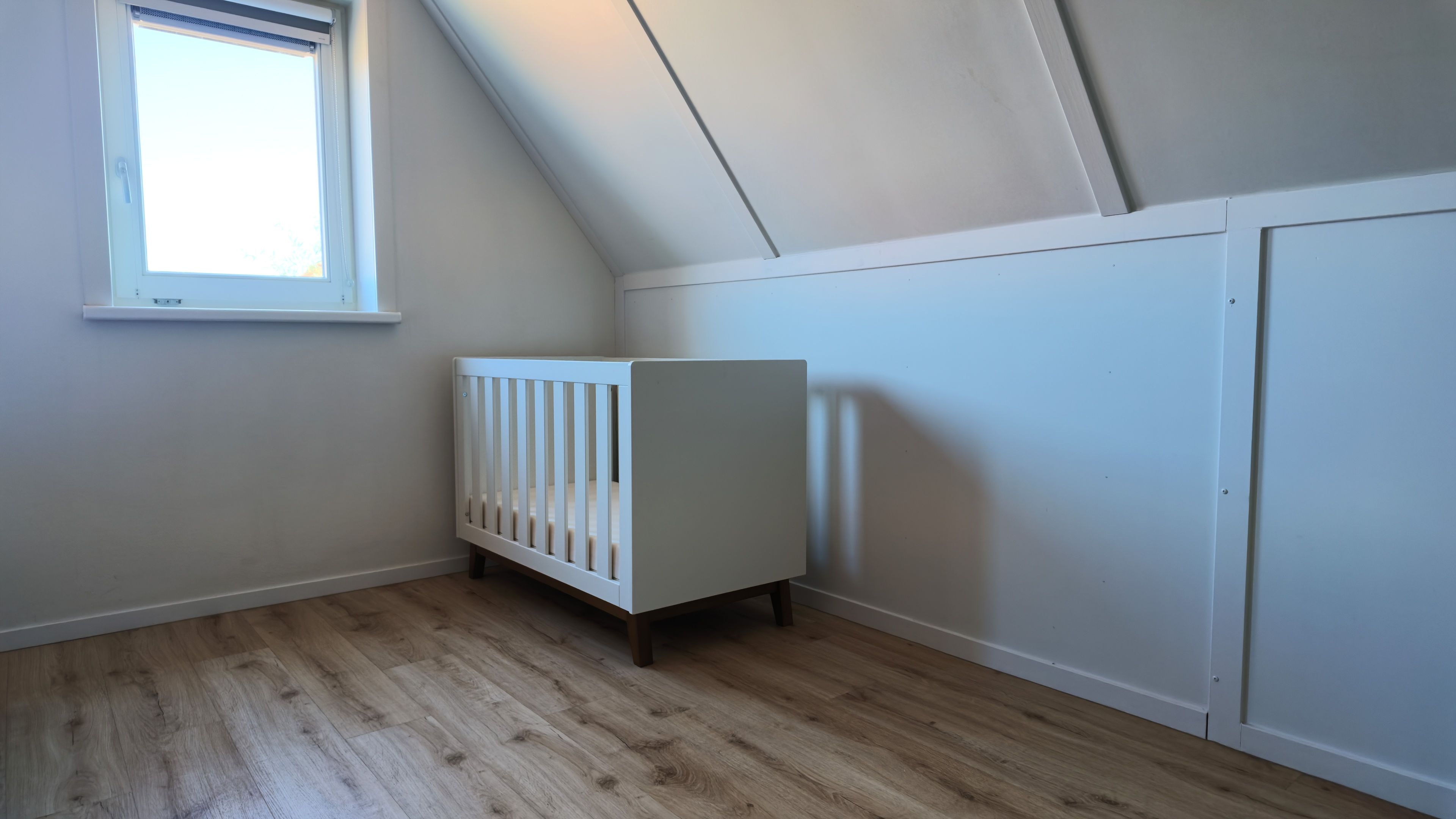 Een kamer met een schuine kap, een wit ledikant en een raam.