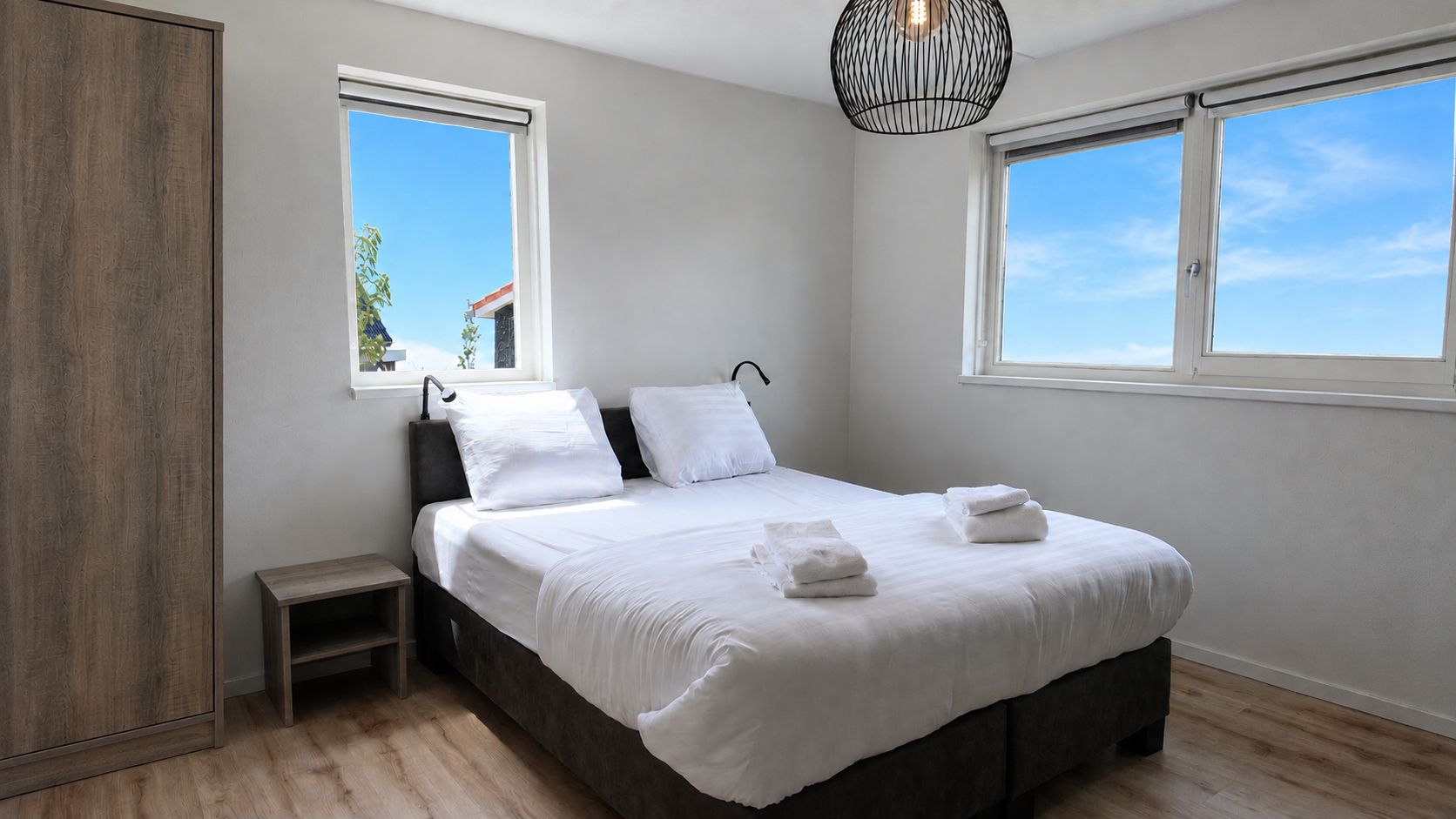 Una camera da letto con un letto, due finestre, un comodino e una lampada a sospensione.