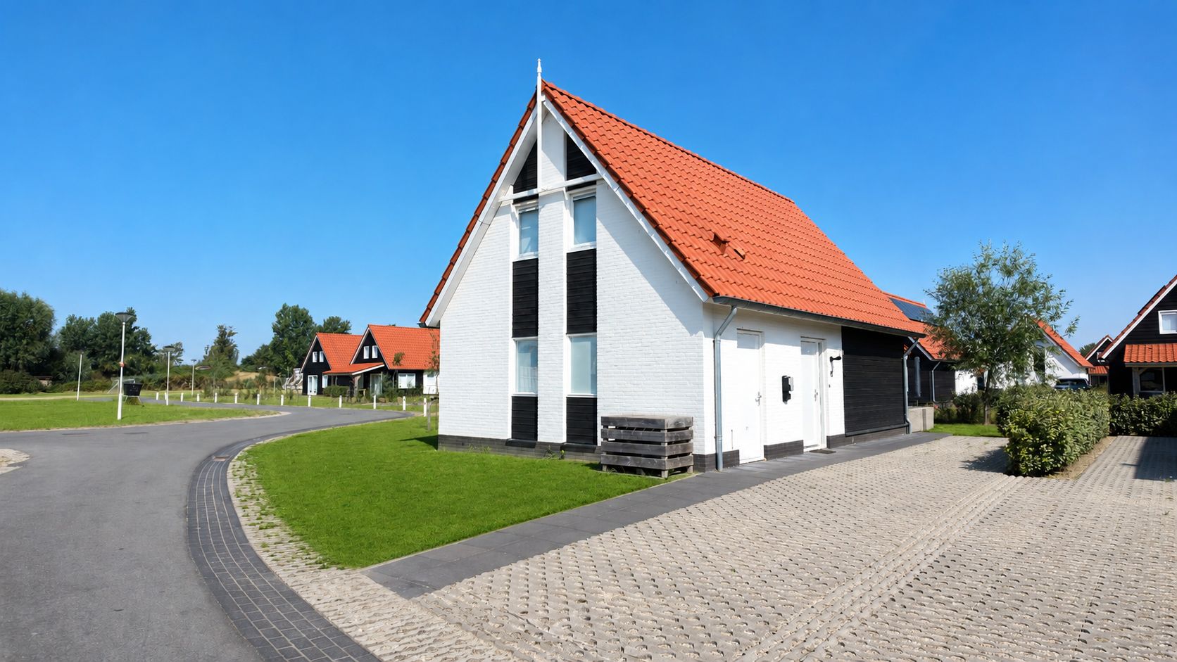 Een woongebouw met een rode pannendak, witte buitenmuren en een geplaveid pad.