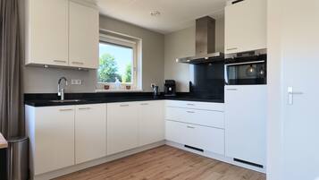 Une cuisine moderne avec des meubles blancs, un plan de travail noir et une fenêtre donnant sur les arbres.