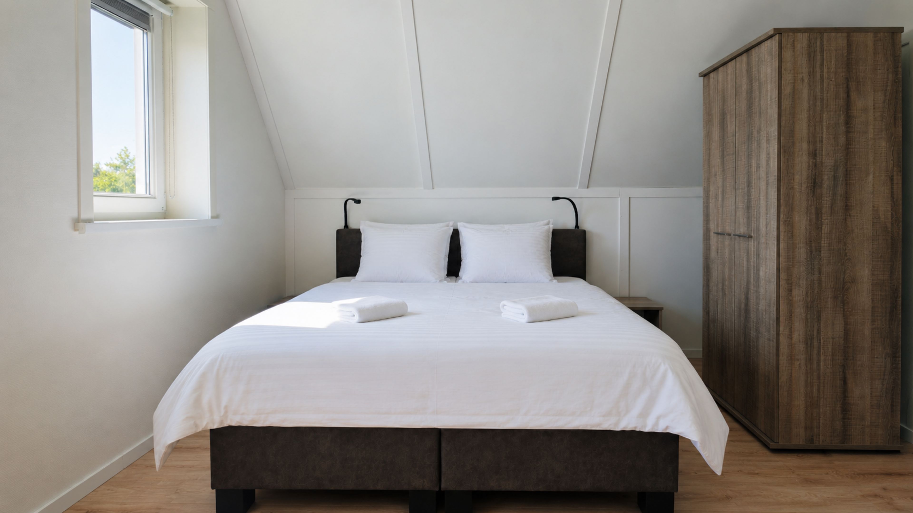 Une chambre à coucher avec un lit, des oreillers, une table de chevet, une armoire et une fenêtre.
