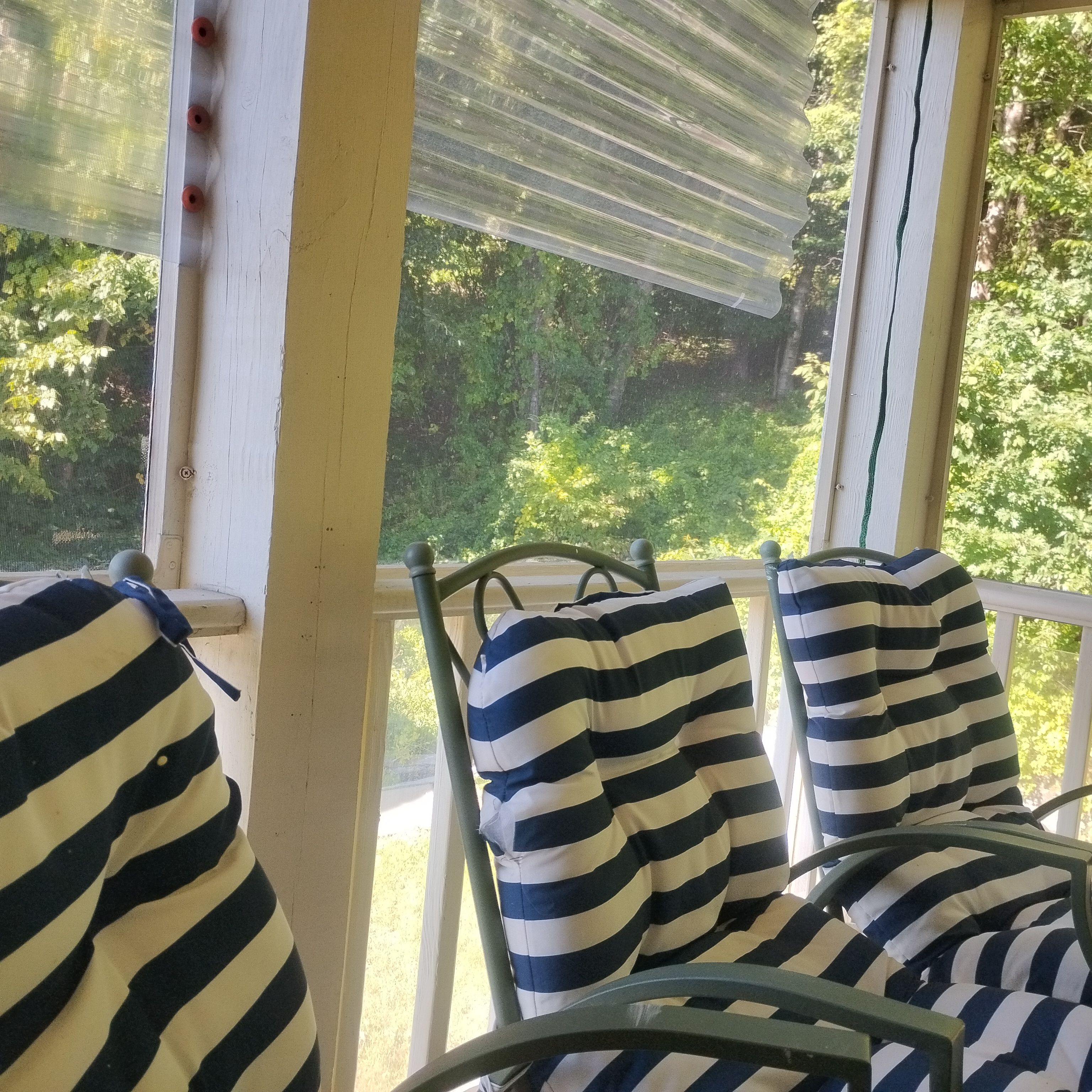 A porch with metal chairs and a striped cushion, overlooking a green landscape.