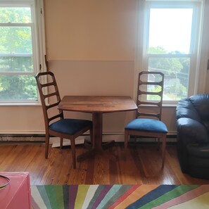 Ein Zimmer mit einem Holztisch, zwei Stühlen, einer schwarzen Ledersofa und Blick durch große Fenster.