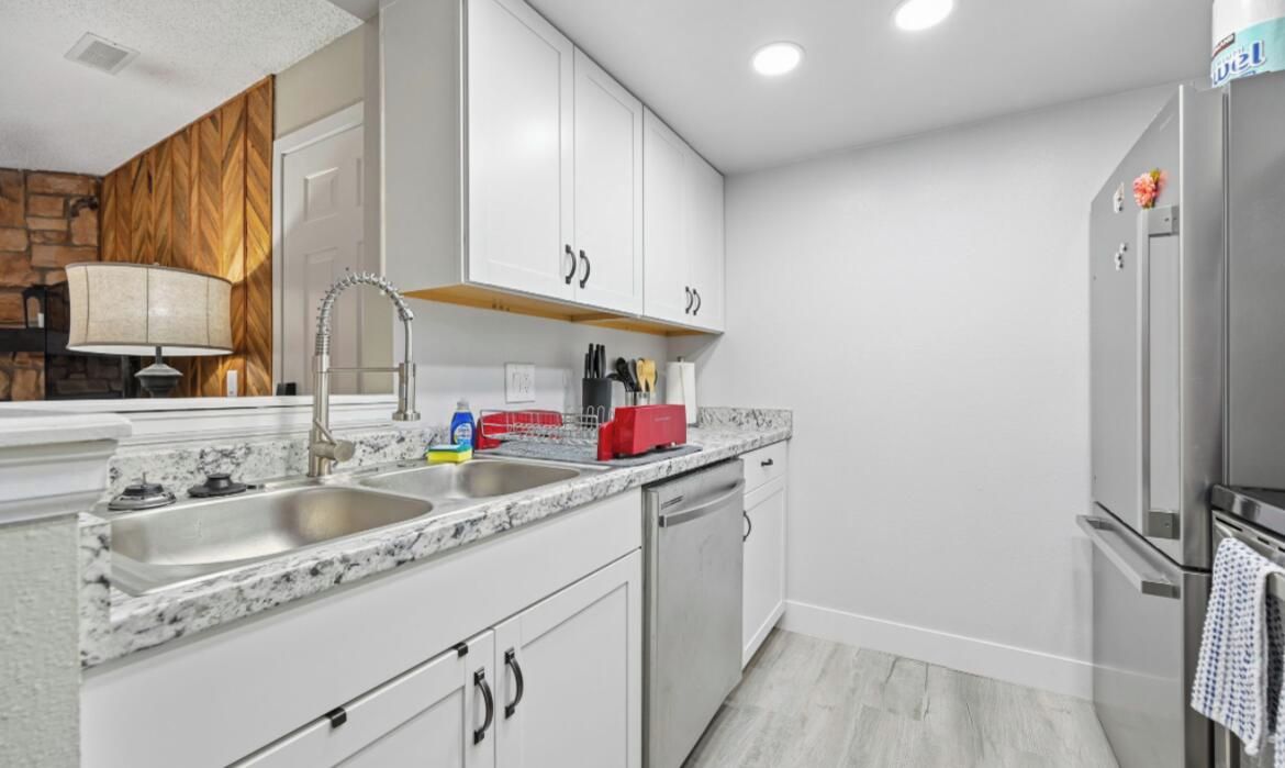 Una cocina moderna con gabinetes blancos, encimera de granito, electrodomésticos de acero inoxidable y horno empotrado.