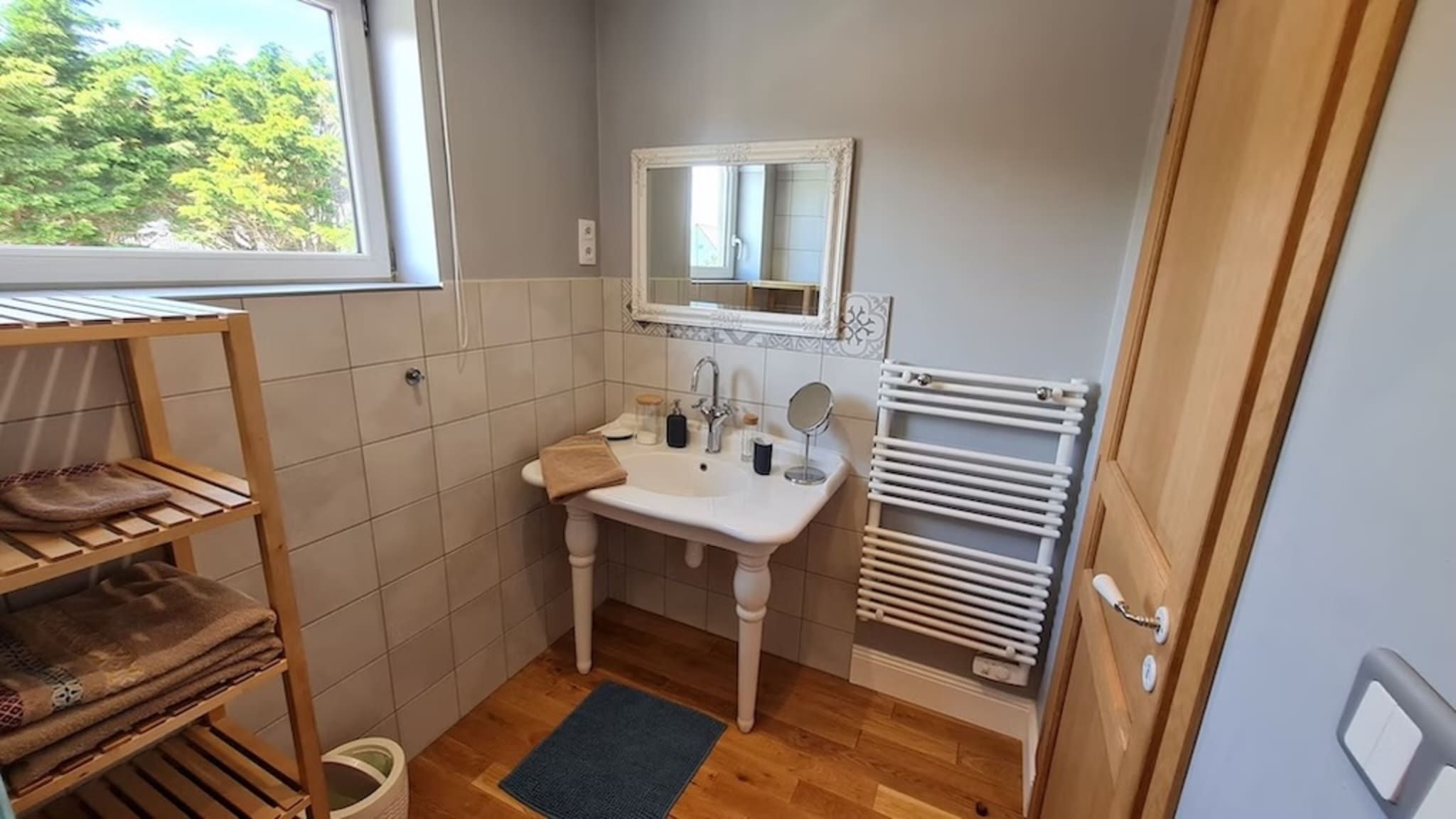 Une petite salle de bain comprenant un lavabo sur colonne, un miroir, un porte-serviettes et une fenêtre.