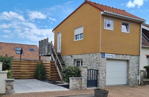 A two-story residential building with a garage, a wooden fence, and a stone wall. - Studio Ô de Mer - 20 meters from the beach in Sangatte (Sangatte)