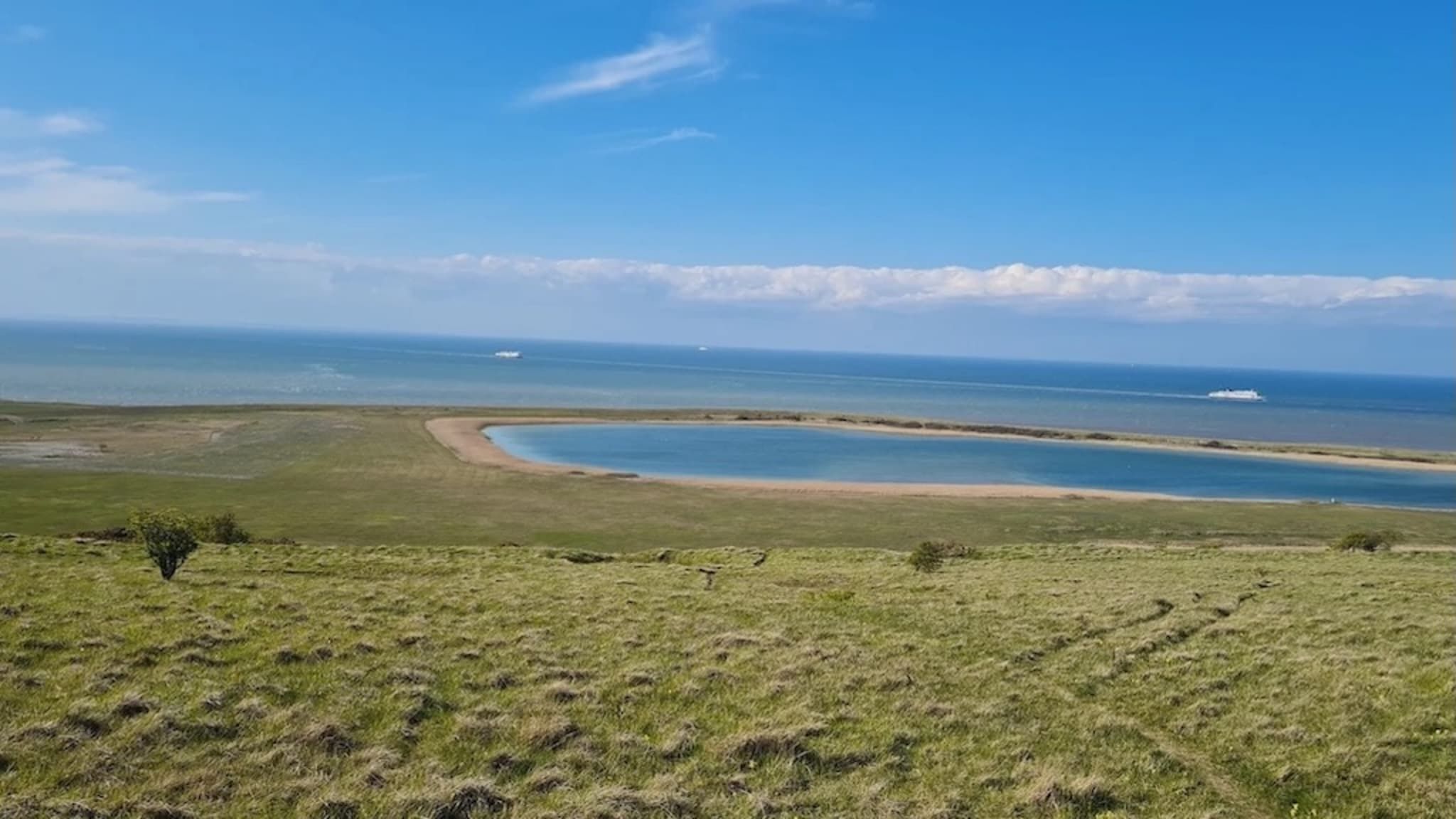 Un paysage côtier avec une baie en forme de courbe, un terrain herbeux et un ciel dégagé.